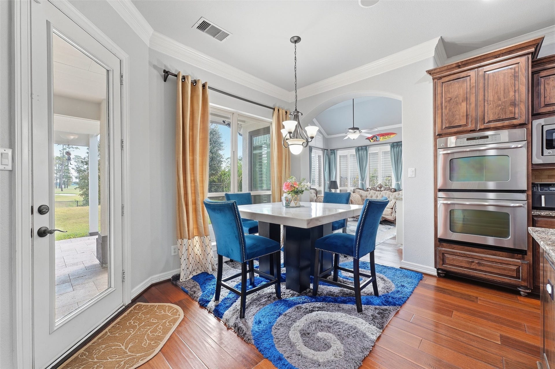 8311 Caroline Ridge Drive, Humble, TX 77396 Bright dining area with stylish blue chairs, a modern light fixture, and large windows offering scenic views, seamlessly connecting to an inviting living room and gourmet kitchen with stainless steel appliances.