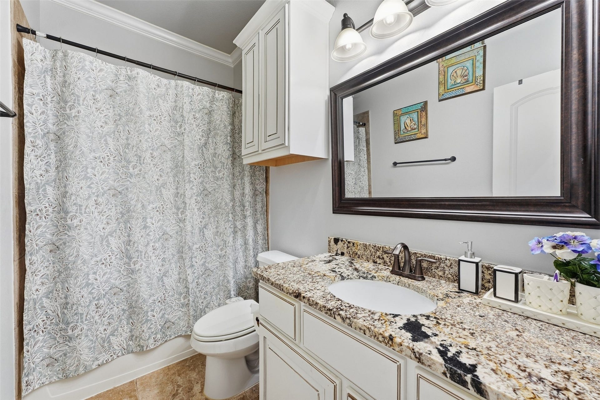 8311 Caroline Ridge Drive, Humble, TX 77396 Charming bathroom featuring a granite countertop, elegant cabinetry, and a stylishly patterned shower curtain, accented by a large framed mirror and modern lighting.
