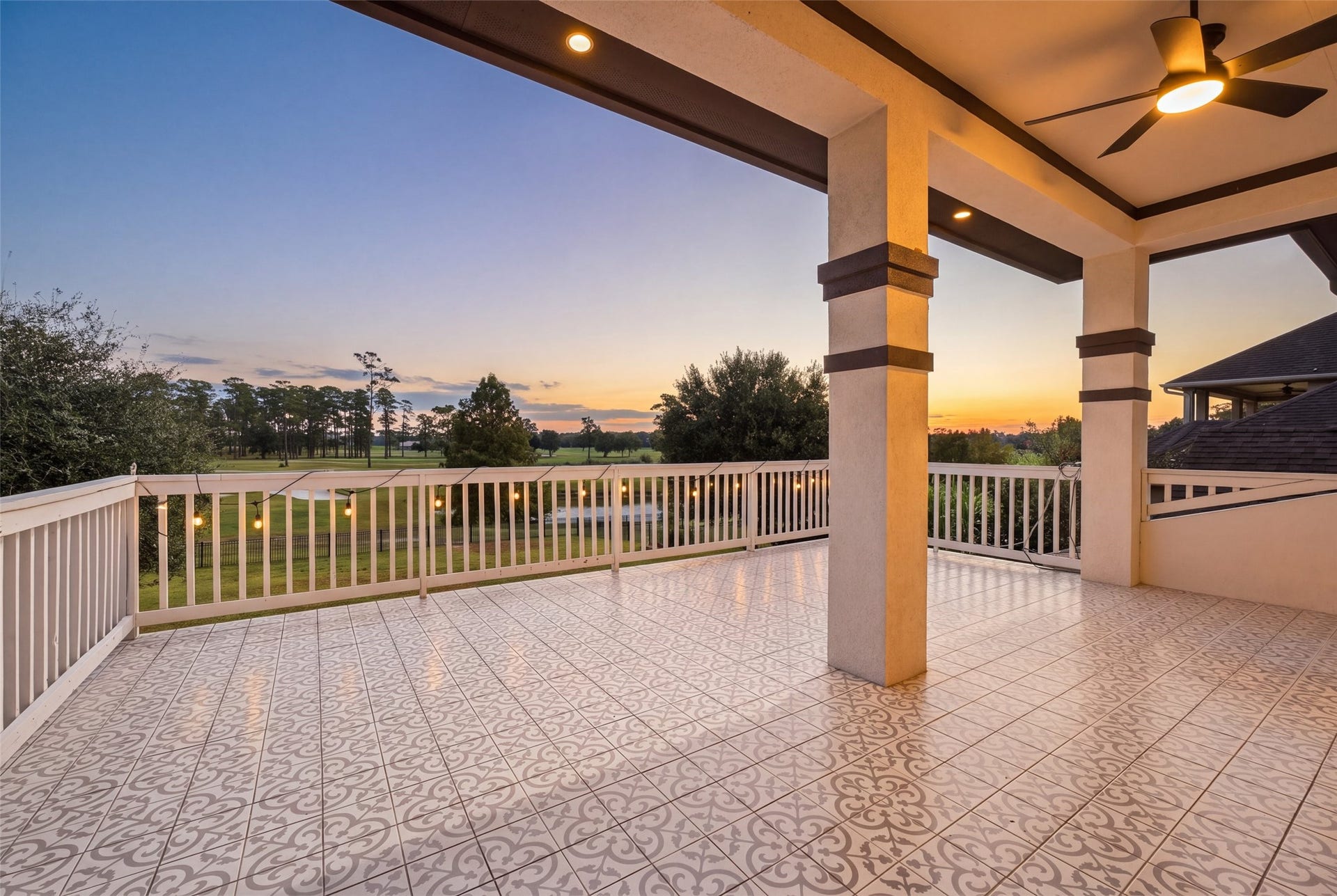 8311 Caroline Ridge Drive, Humble, TX 77396 Expansive covered balcony with elegant tile flooring and ceiling fans offers stunning sunrise views over a lush landscape.