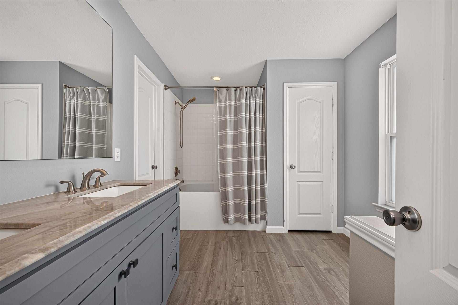 18019 Rexine Lane, Cypress, TX 77433 Elegant bathroom featuring a stylish vanity with a marble countertop, a classic tub-shower combo with a patterned curtain, and vinyl plank flooring, all in a soothing neutral palette.