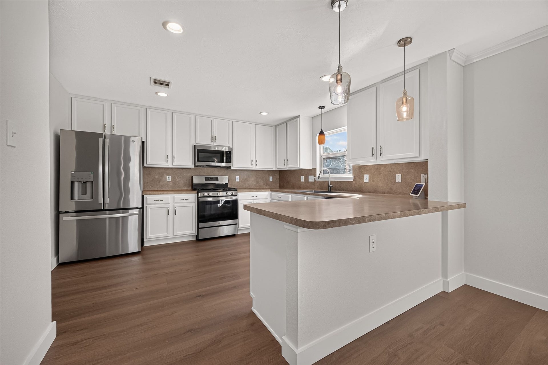 18019 Rexine Lane, Cypress, TX 77433 Spacious kitchen with stainless steel appliances, white cabinetry, and sleek pendant lighting, complemented by a warm vinyl plank floor and ample counter space for cooking and entertaining.