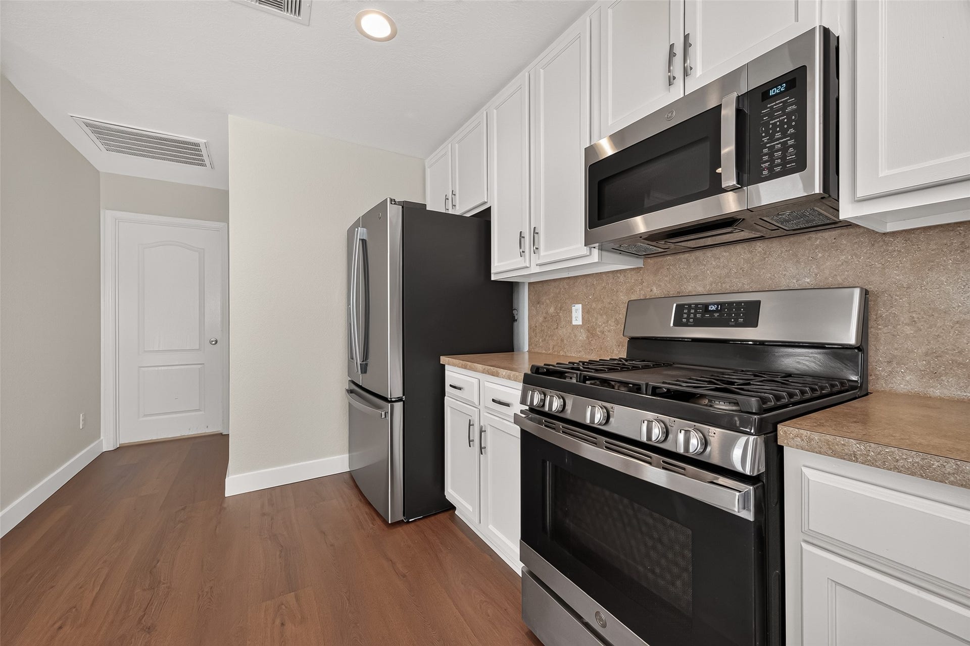 18019 Rexine Lane, Cypress, TX 77433 Modern kitchen with stainless steel appliances, sleek white cabinetry, and rich vinyl plank flooring, creating a stylish and functional space.