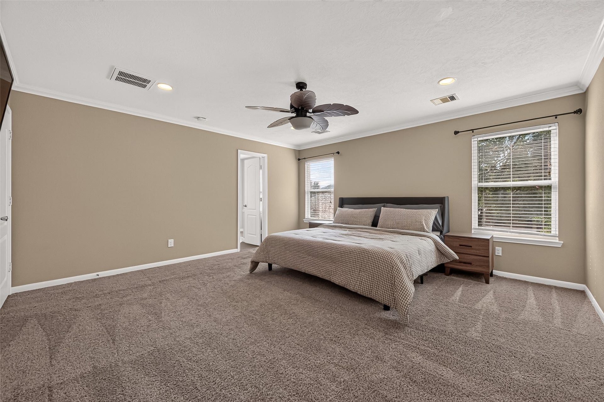 18019 Rexine Lane, Cypress, TX 77433 Spacious primary bedroom featuring cozy carpeting, neutral walls, and ample natural light from dual windows, complete with an elegant ceiling fan and ensuite access.