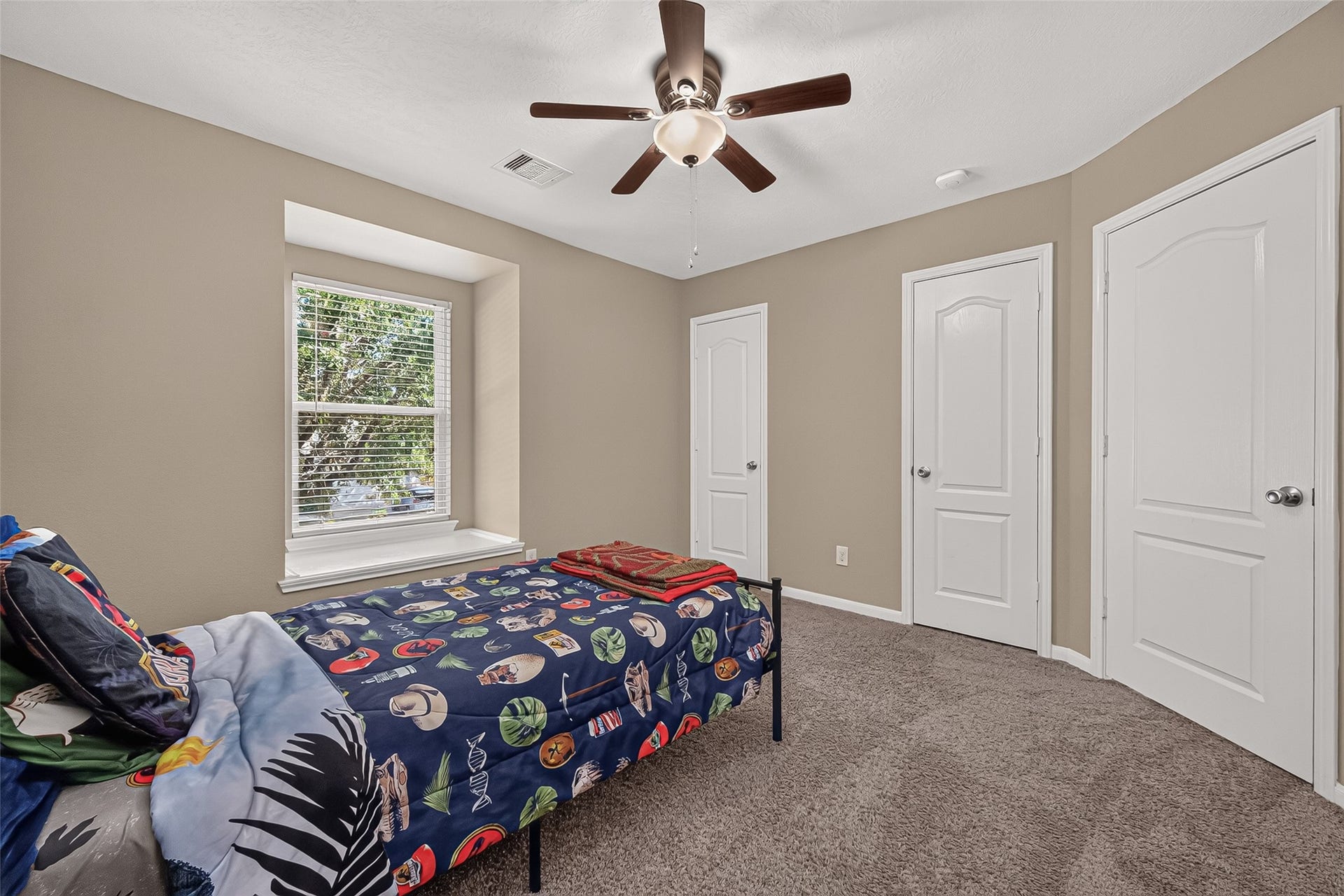 18019 Rexine Lane, Cypress, TX 77433 Cozy secondary bedroom with neutral tones, featuring a large window for natural light, plush carpeting, and a ceiling fan for comfort.