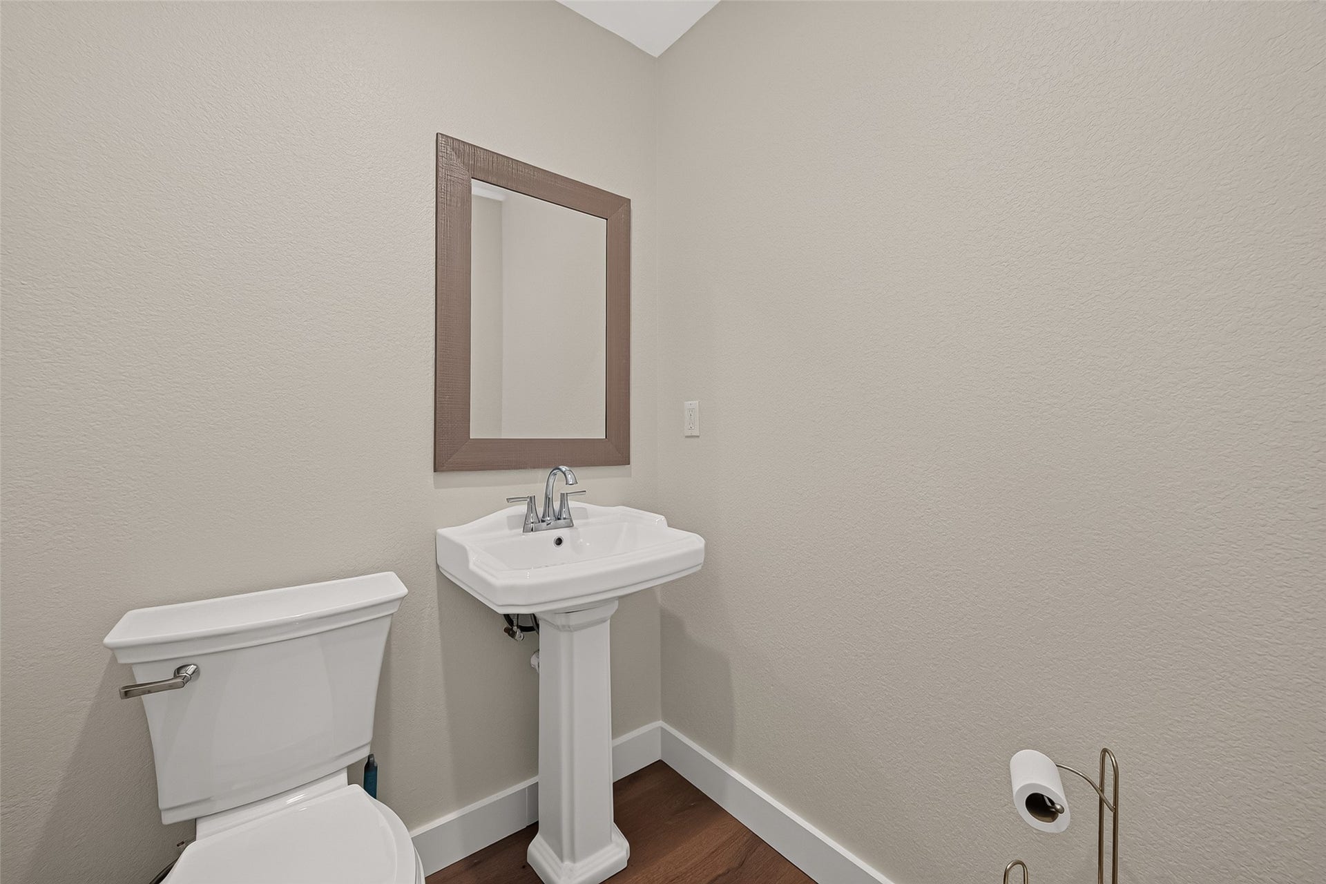 18019 Rexine Lane, Cypress, TX 77433 Charming powder bath featuring a sleek pedestal sink, elegant framed mirror, and warm vinyl plank flooring for a cozy touch.