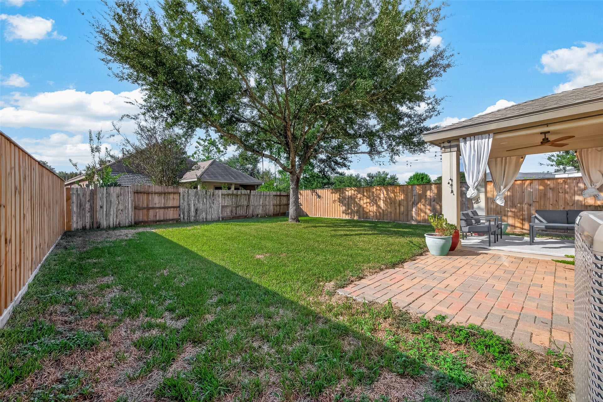 18019 Rexine Lane, Cypress, TX 77433 Charming backyard featuring a spacious patio with a cozy seating area under a covered pergola, complemented by lush green grass and a beautiful mature tree. Perfect for outdoor relaxation and entertaining.
