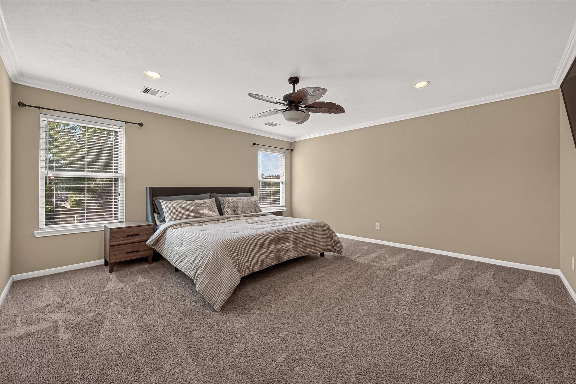 18019 Rexine Lane, Cypress, TX 77433 Spacious primary bedroom featuring neutral tones, plush carpeting, and ample natural light from two large windows, complete with a modern ceiling fan for comfort.
