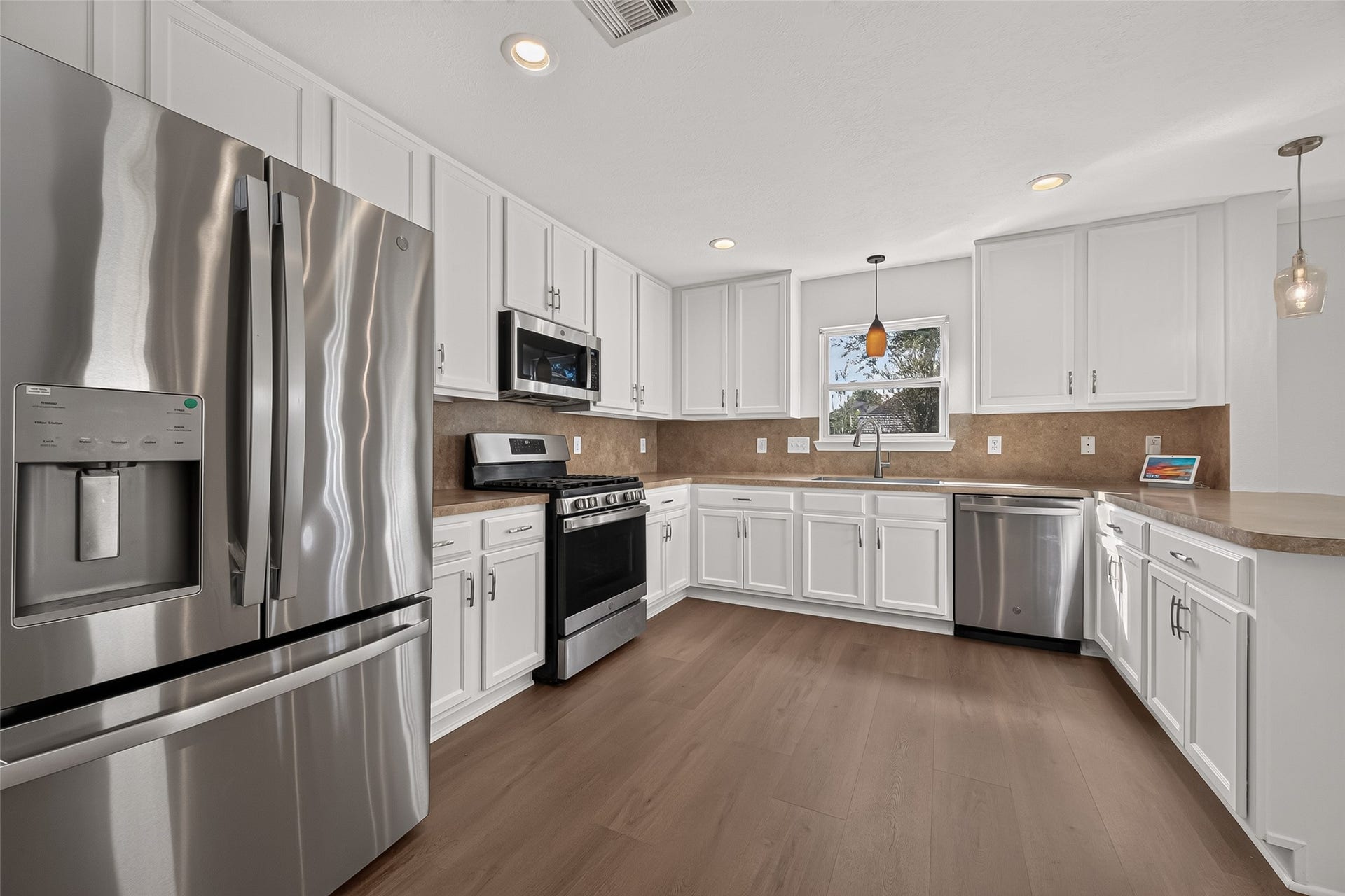 18019 Rexine Lane, Cypress, TX 77433 Spacious kitchen with stainless steel appliances, white cabinetry, and sleek pendant lighting, complemented by a warm vinyl plank floor and ample counter space for cooking and entertaining.
