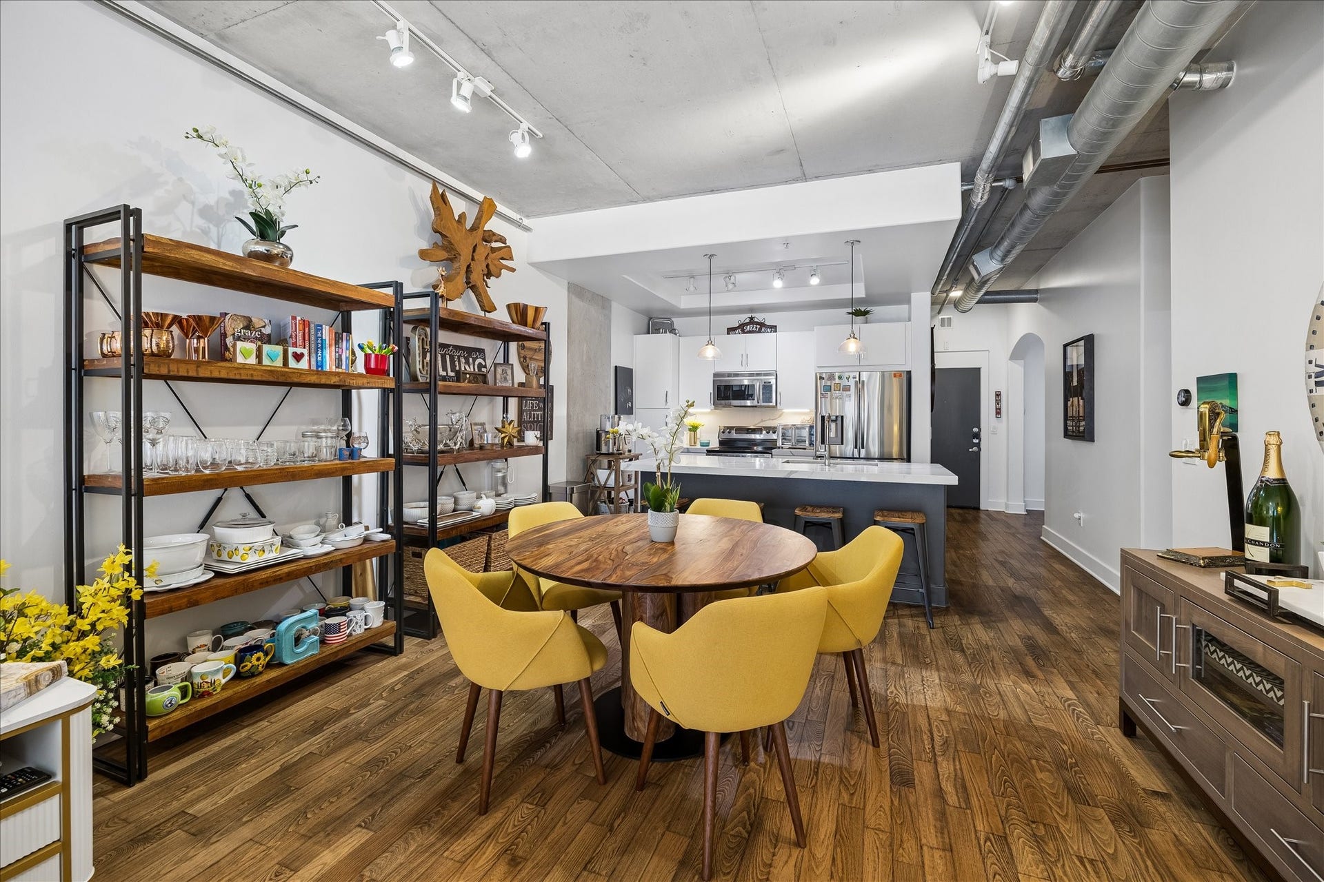 Stylish open-plan dining and kitchen area featuring sleek hardwood floors, vibrant yellow chairs, and industrial accents, perfect for modern living and entertaining.