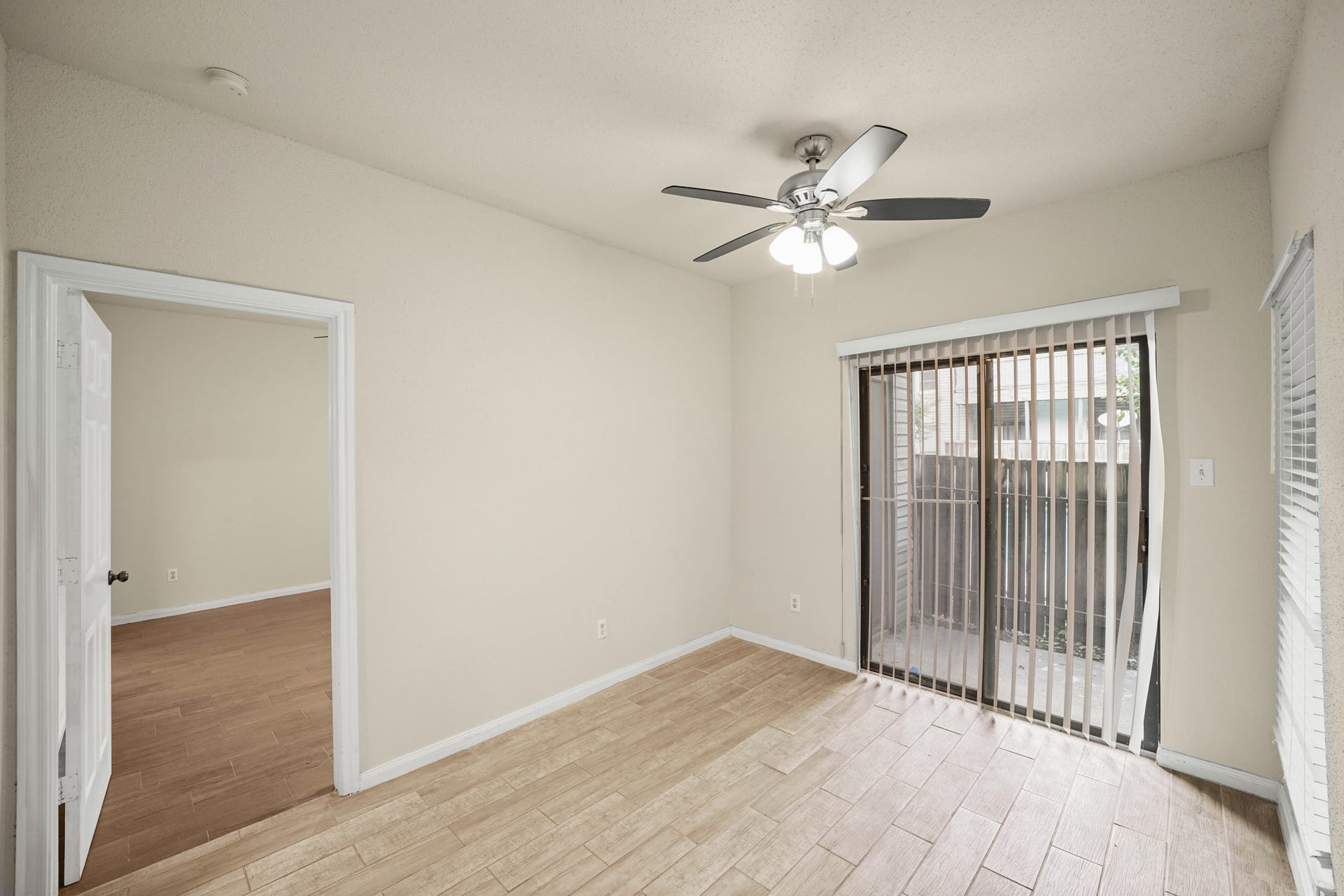 Dining area with glass sliding door that leads to back fenced patio area.  It has a ceiling fan with lights. Open door way leads to the bedroom.