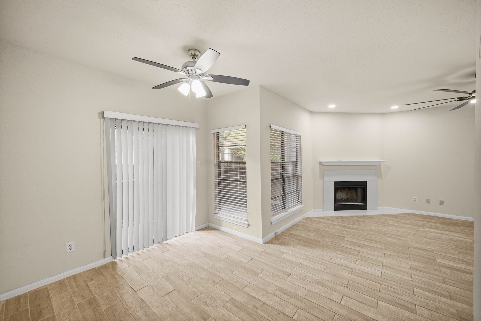 View of the living area and dining area. Fireplace in living area, and ceiling fans for comfort. Natural light pours in through large windows and sliding glass doors that lead to a fenced patio area.