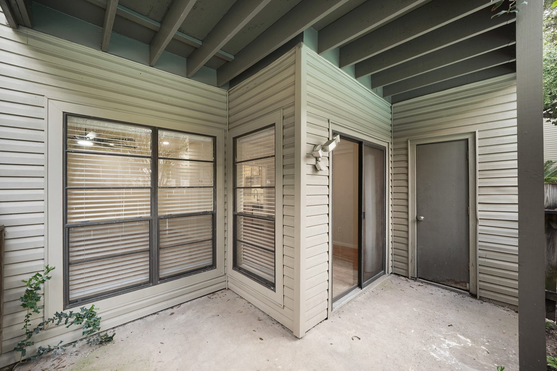 Small, covered patio area featuring sliding glass doors and large windows that allow natural light to enter. It offers a private outdoor space with unless potential.