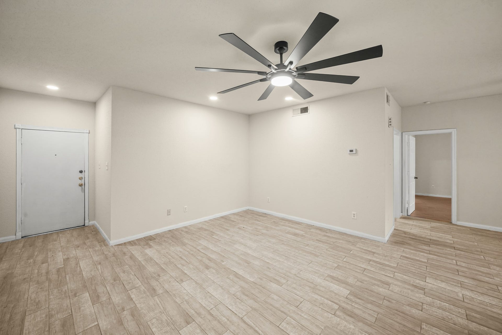 Spacious, modern living area features recessed lighting, a large ceiling fan, and an open doorway leading to the bedroom.