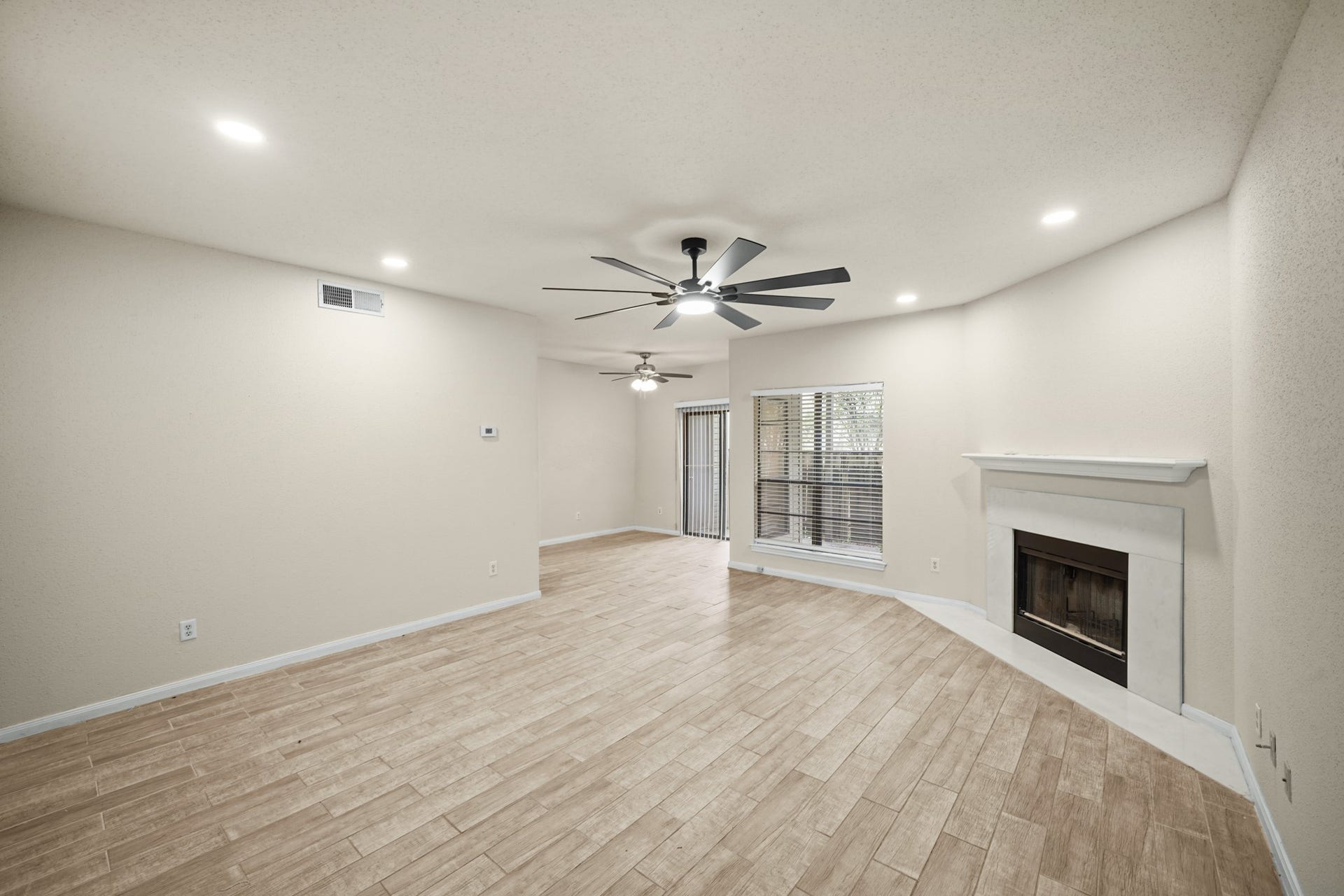 Living area features a modern ceiling fan, recessed lighting, and a cozy fireplace.  Large windows allow for natural light, with sliding doors leading to a fenced patio area.