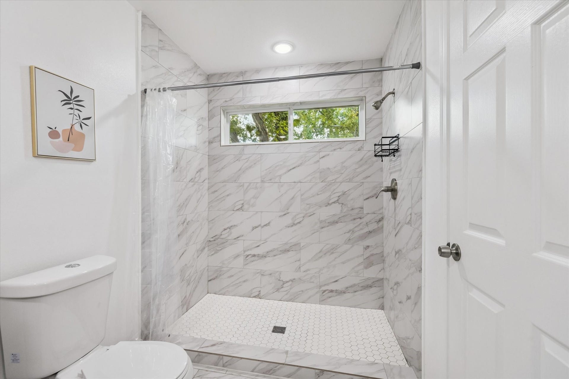 2631 Stevens Street, Houston, TX 77026 The primary bathroom features a spacious walk-in shower with floor-to-ceiling marble-look tile and white hexagon tile flooringelevating both style and function.