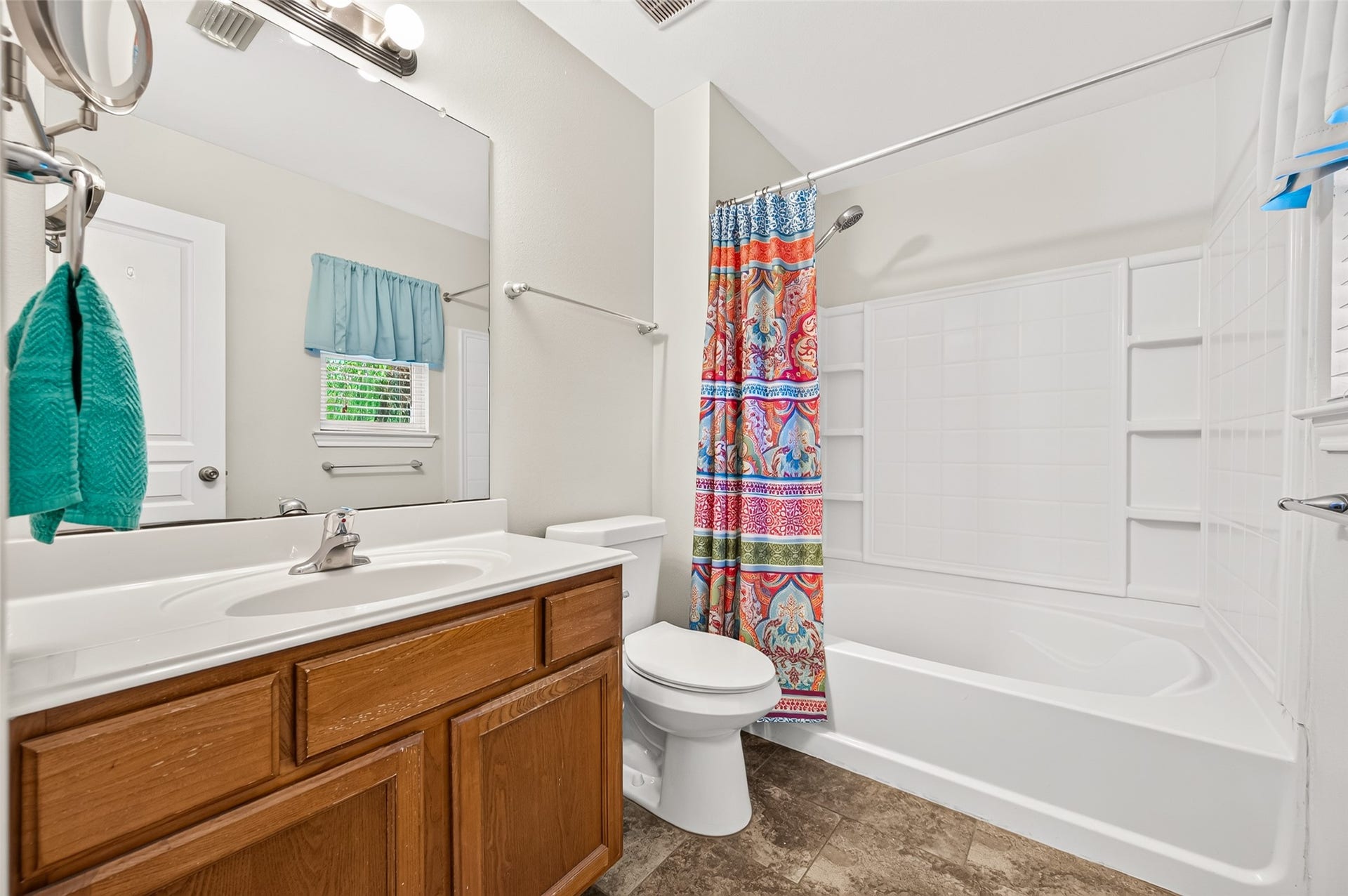 The primary bathroom features a spacious vanity, large mirror, garden size-tub/shower combination with built-in shelving, tile flooring installed in 2023, and a commode replaced in 2022.