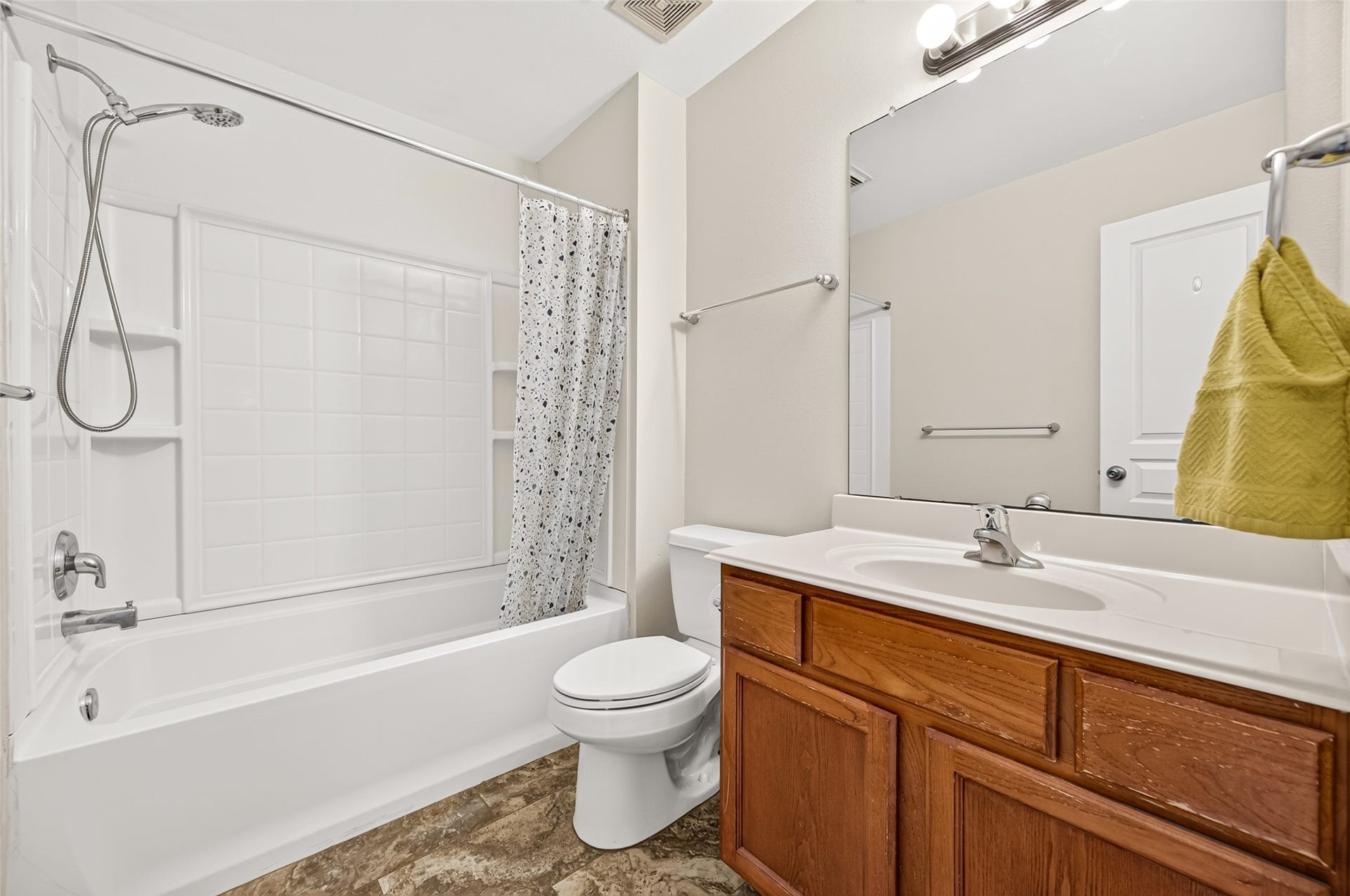 The secondary bathroom offers ample cabinet space, a large mirror, and durable tiled floors. Complete with a tub-and-shower combination and a clean neutral palette, it provides a bright and practical space for everyday routines.