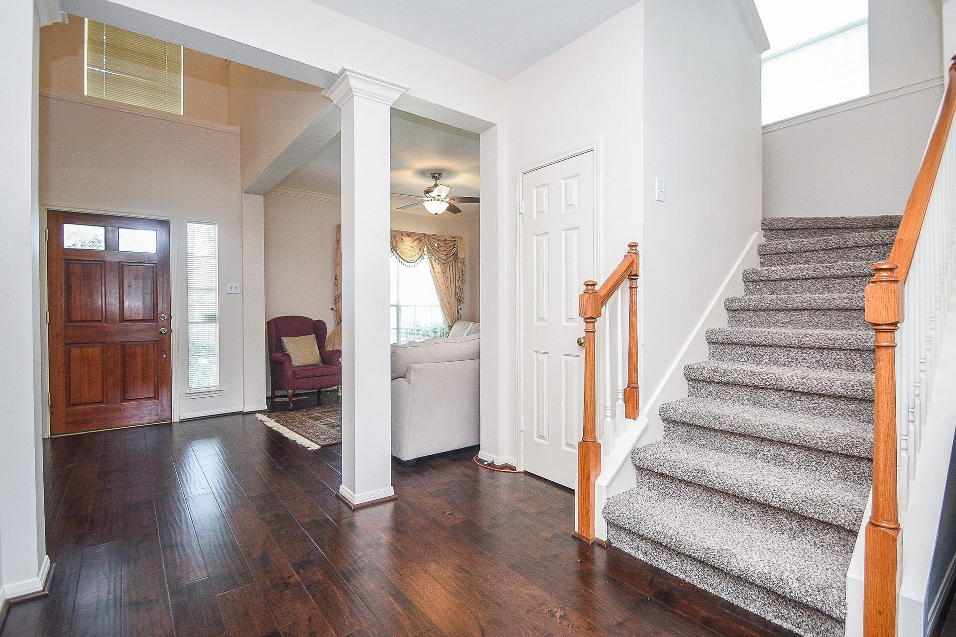 15715 Brookwood Lake Place, Sugar Land, TX 77498 This entryway features beautiful dark hardwood floors, a wooden front door with sidelights, and a carpeted staircase. The space opens into a bright living area with a ceiling fan, offering a warm and inviting atmosphere.