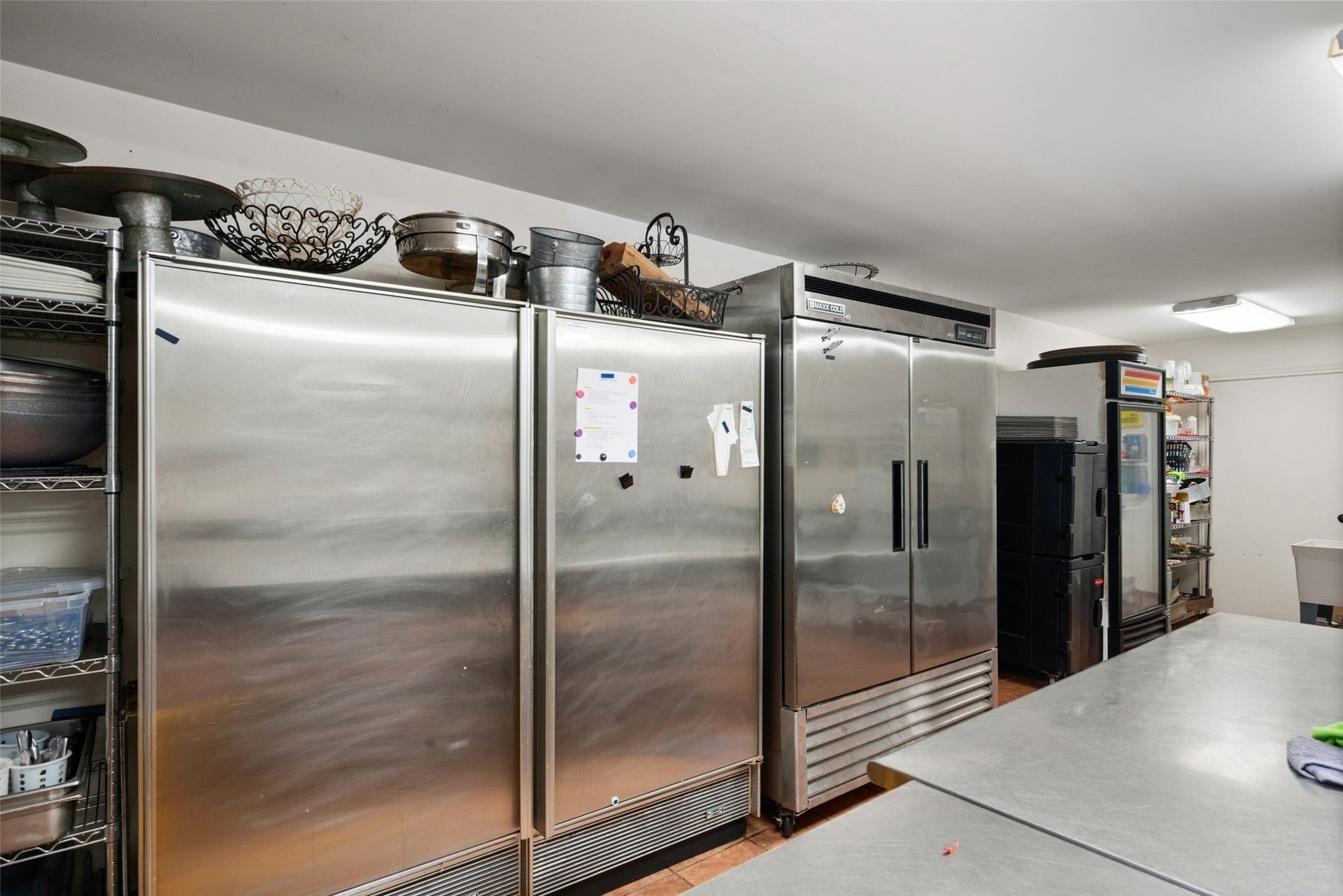 Reception hall kitchen area featuring multiple stainless steel refrigeration units and a large work surface.