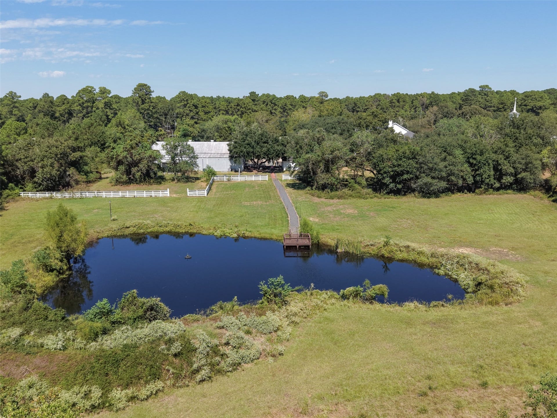 Aerial view showcases the pond with dock, open grassy areas, and surrounding trees, with venue improvements in the distance.