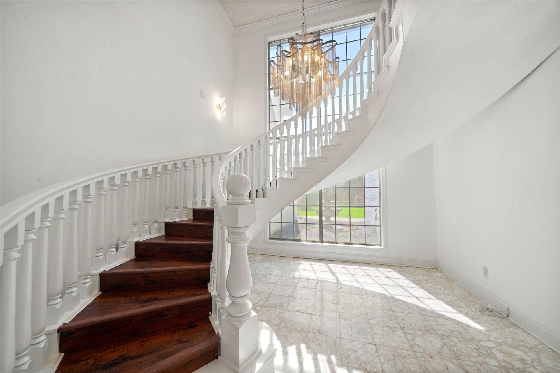 Elegant curved staircase with rich wood treads, white balusters, and a sparkling chandelier creates a striking focal point.
