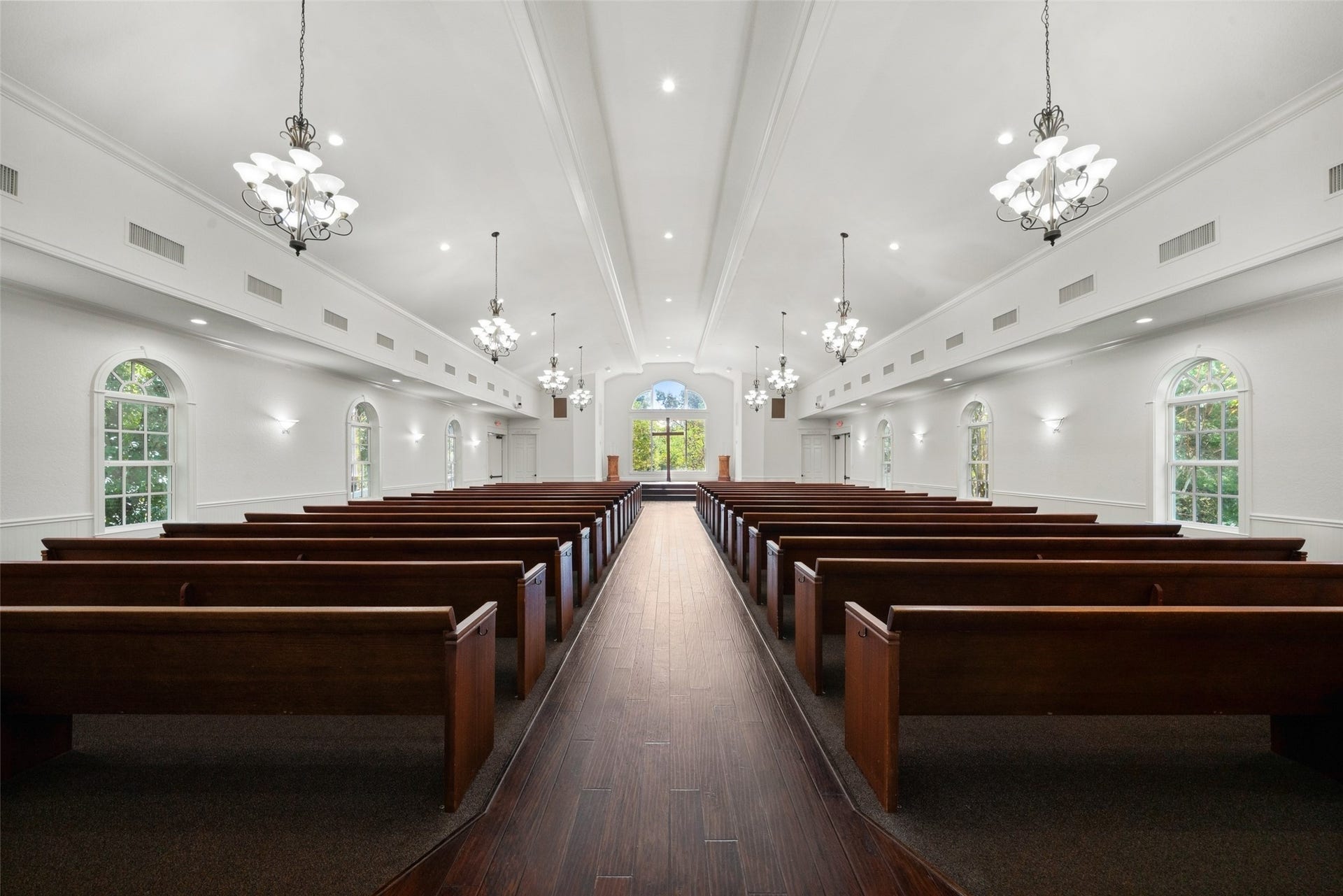Spacious chapel interior features rows of wooden pews, a center aisle, chandeliers, and abundant natural light for weddings and special ceremonies.