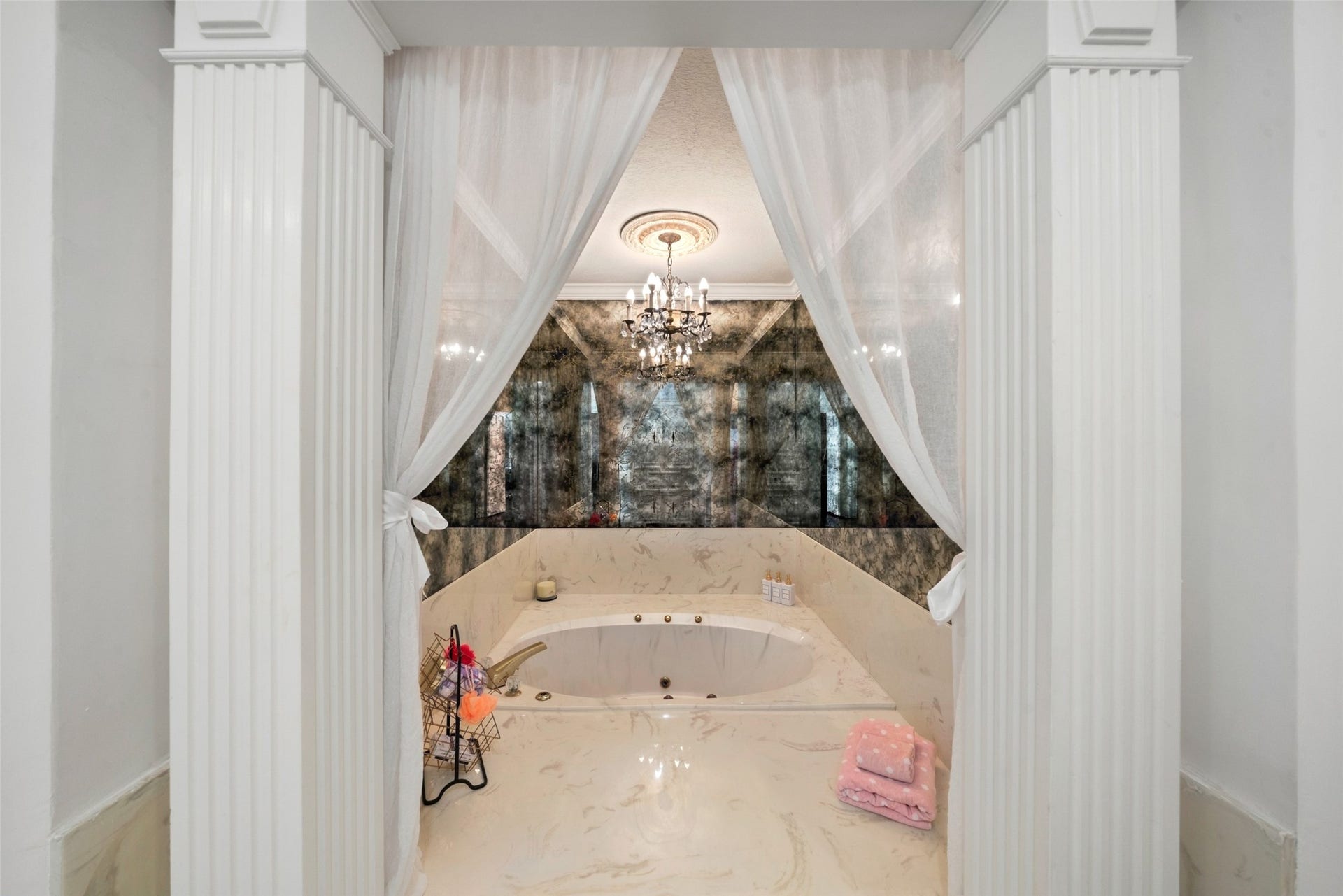 Recessed soaking tub framed by decorative double doors and soft drapery, with a chandelier overhead.