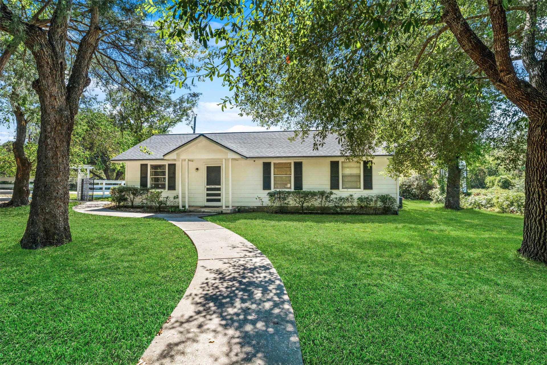 Guest house front exterior featuring a covered porch, a curved walkway, and a spacious lawn shaded by mature trees.