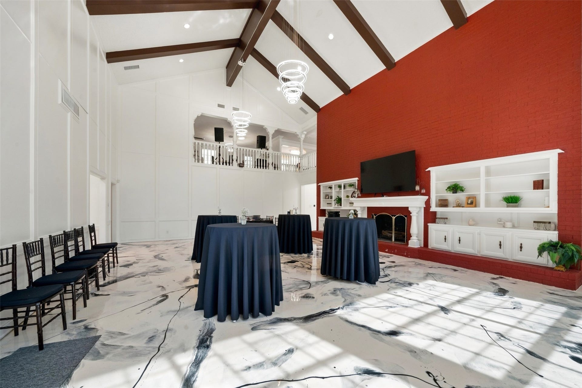 Spacious gathering area with vaulted ceilings, exposed beams, chandeliers, a red accent wall, and room for varied seating arrangements.