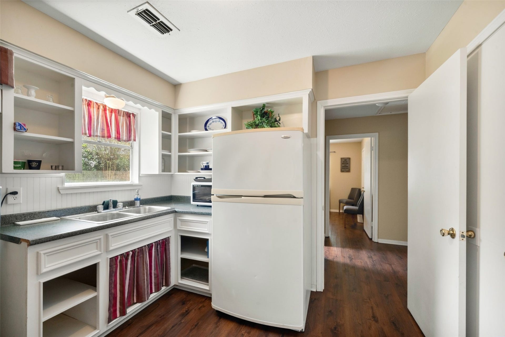 Guest house kitchen featuring a window above the sink, upper and lower cabinetry, a range, and a refrigerator.