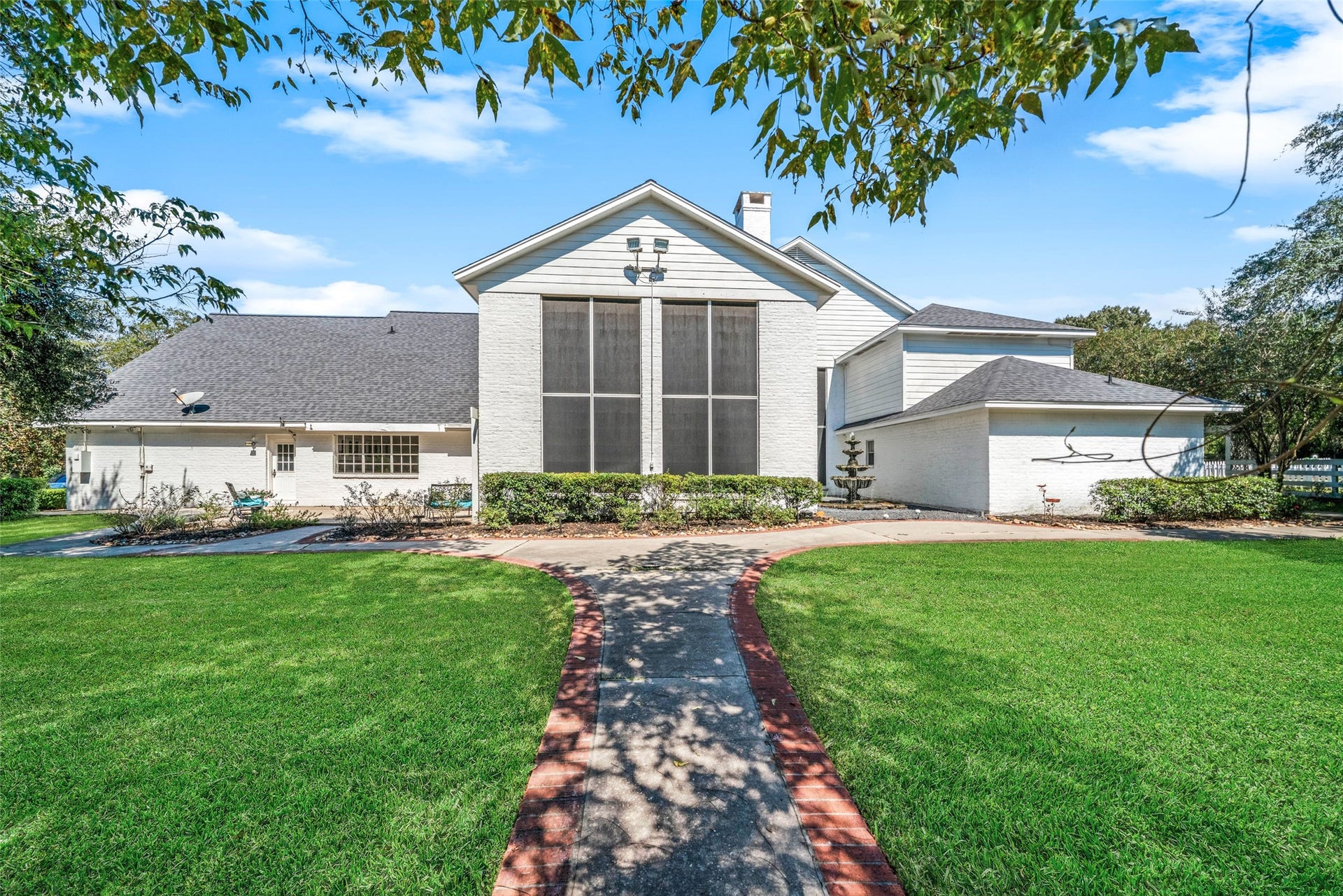 Rear exterior featuring a spacious raised deck, a central wall of windows, and a landscaped walkway bordered by lawn and mature trees.