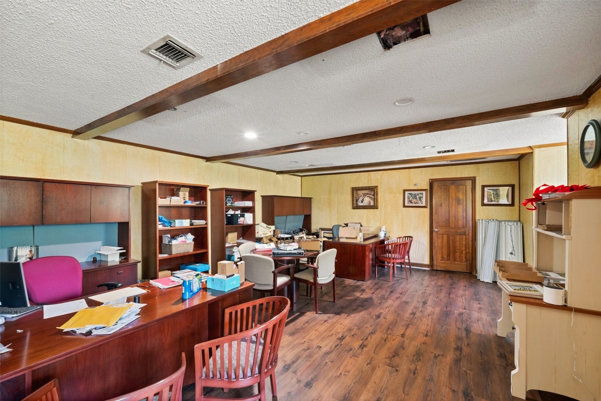 Upstairs office featuring extensive built-in shelving and cabinetry, exposed ceiling beams, wood flooring, and ample room for multiple workstations.