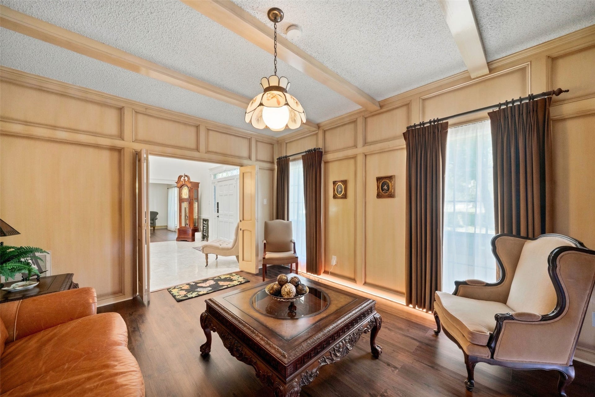Sitting area featuring exposed ceiling beams, a chandelier, wood flooring, and tall windows with drapery.