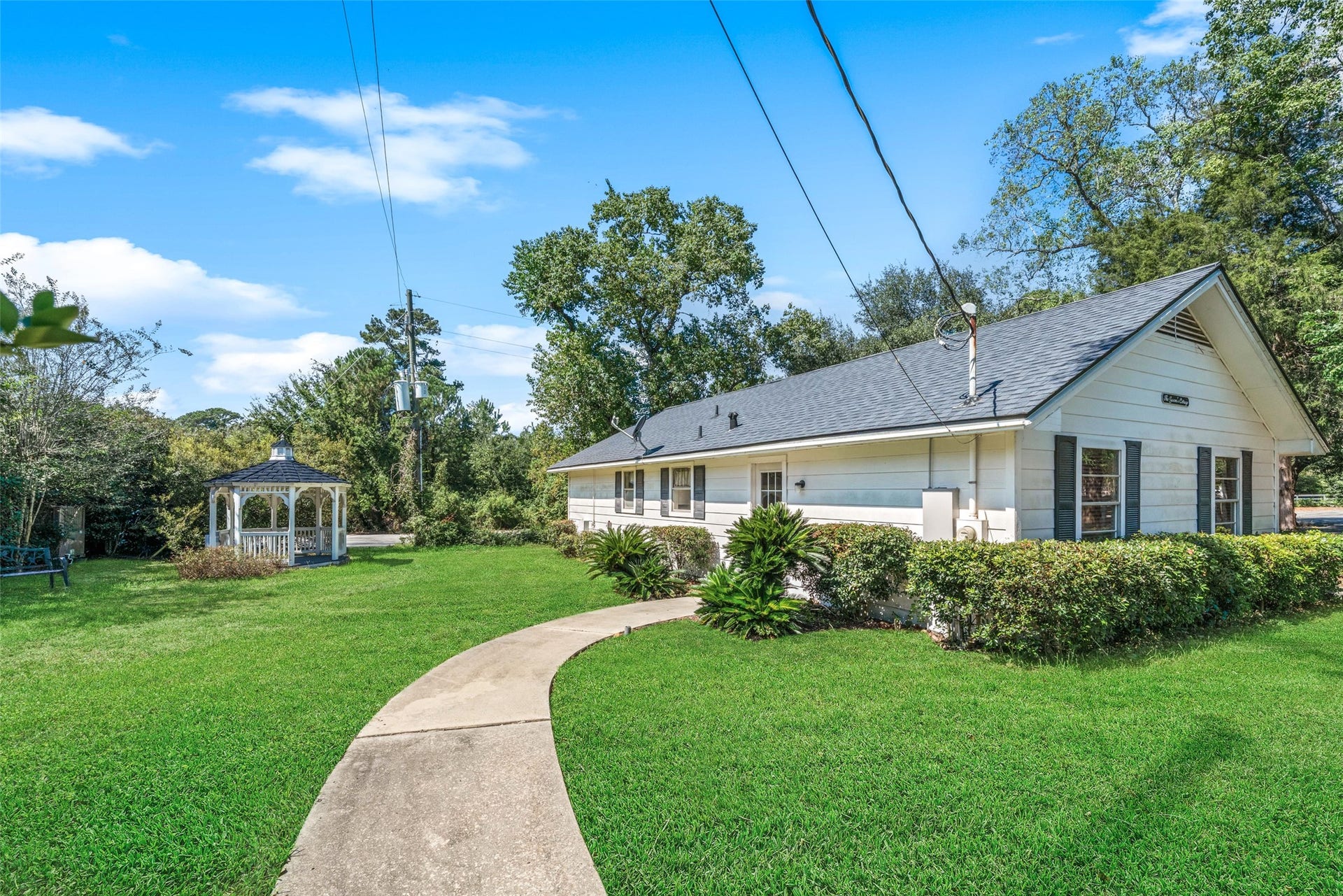 Rear view of the guest house showcasing a covered porch, multiple windows, and surrounding lawn with mature trees and landscaping.