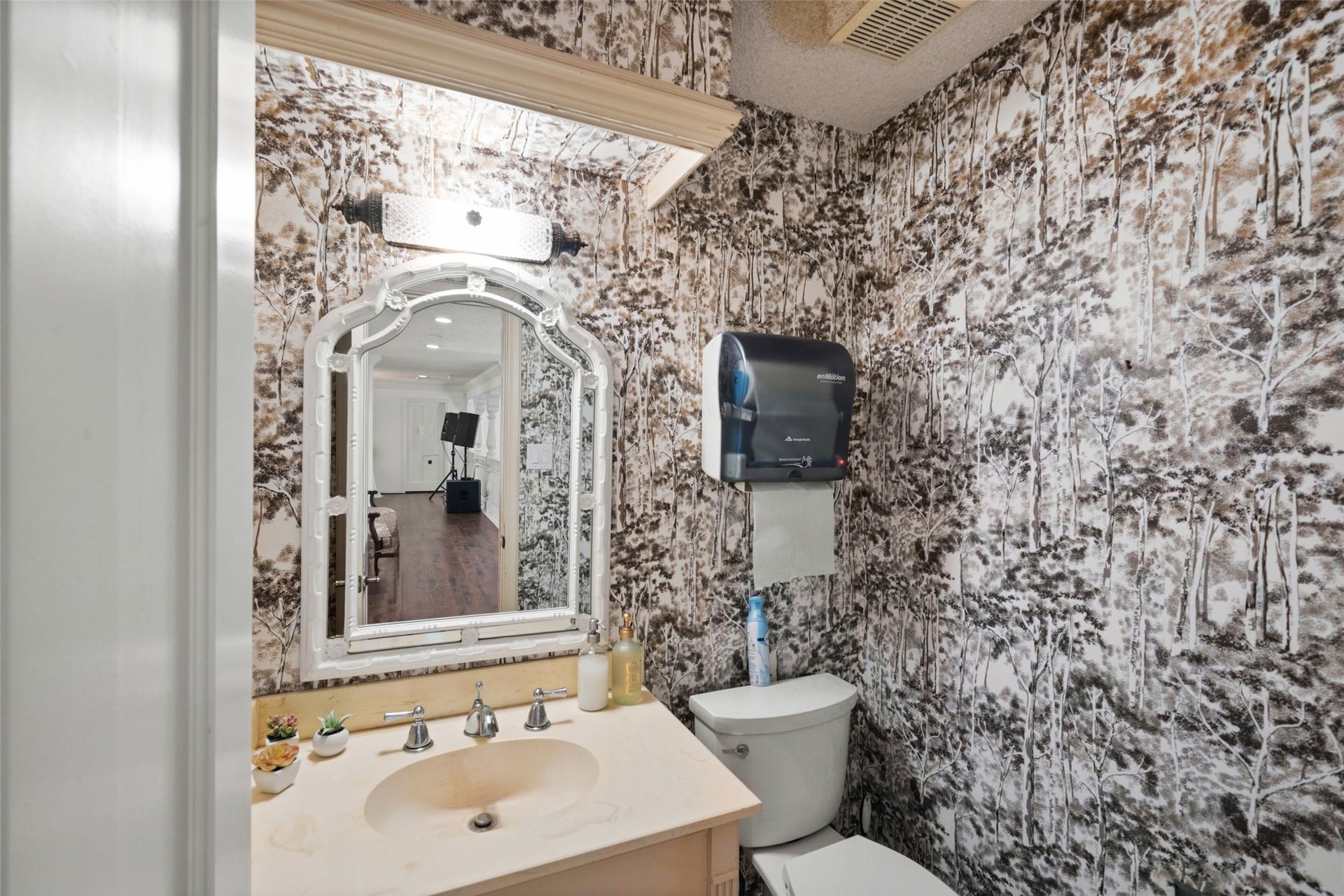 Bathroom with bold patterned wallpaper, an ornate vanity mirror, and decorative lighting.