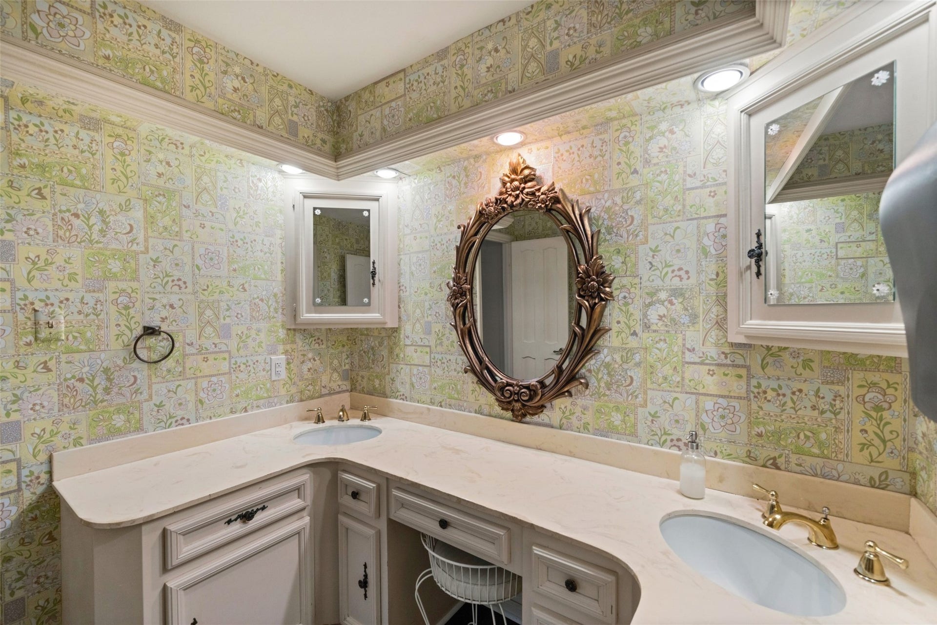 Bathroom featuring an extended vanity, decorative framed mirrors, patterned wall finishes, and ample cabinet storage.
