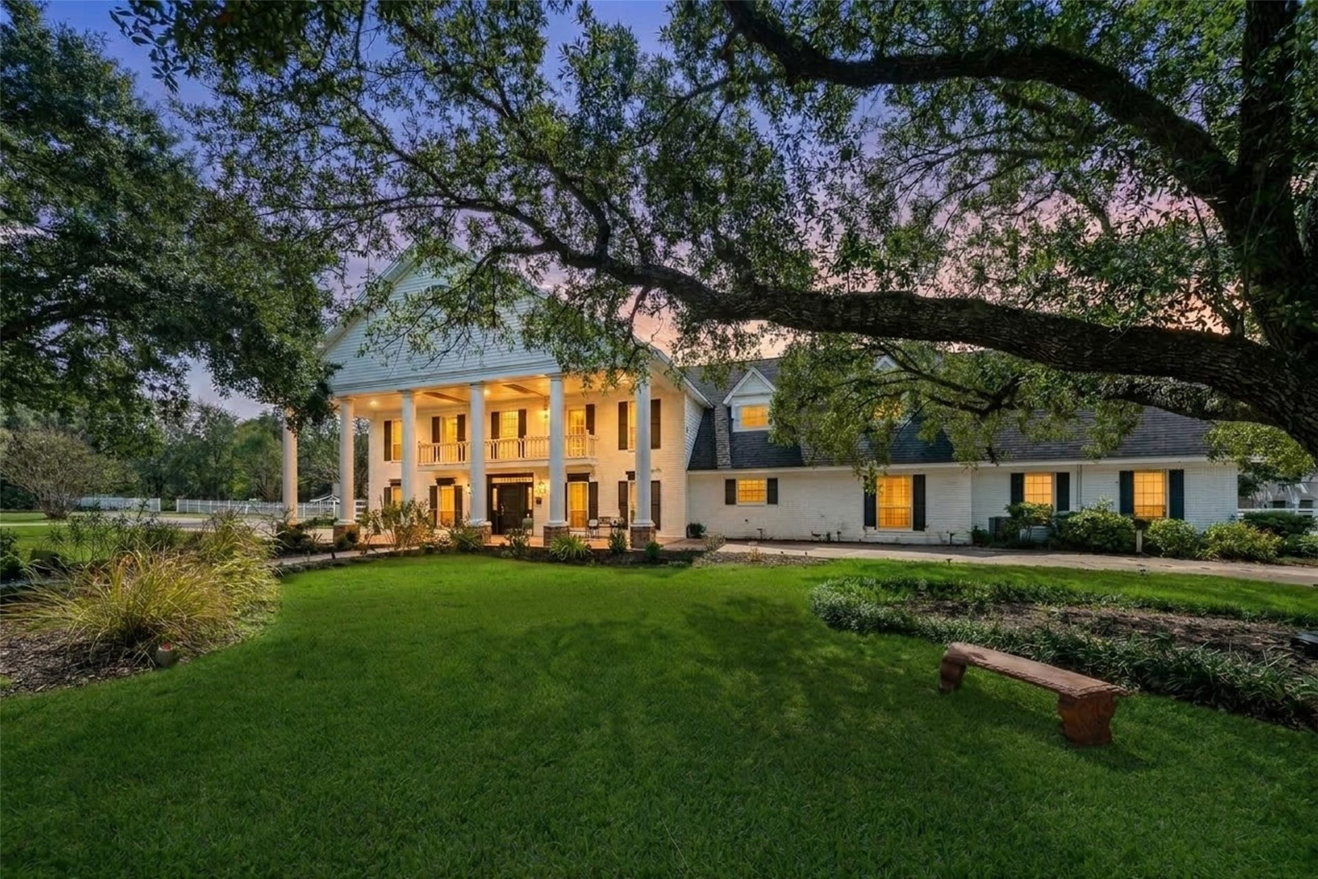 Evening view highlighting the illuminated manor, expansive lawn, and outdoor gathering areas beneath mature shade trees.