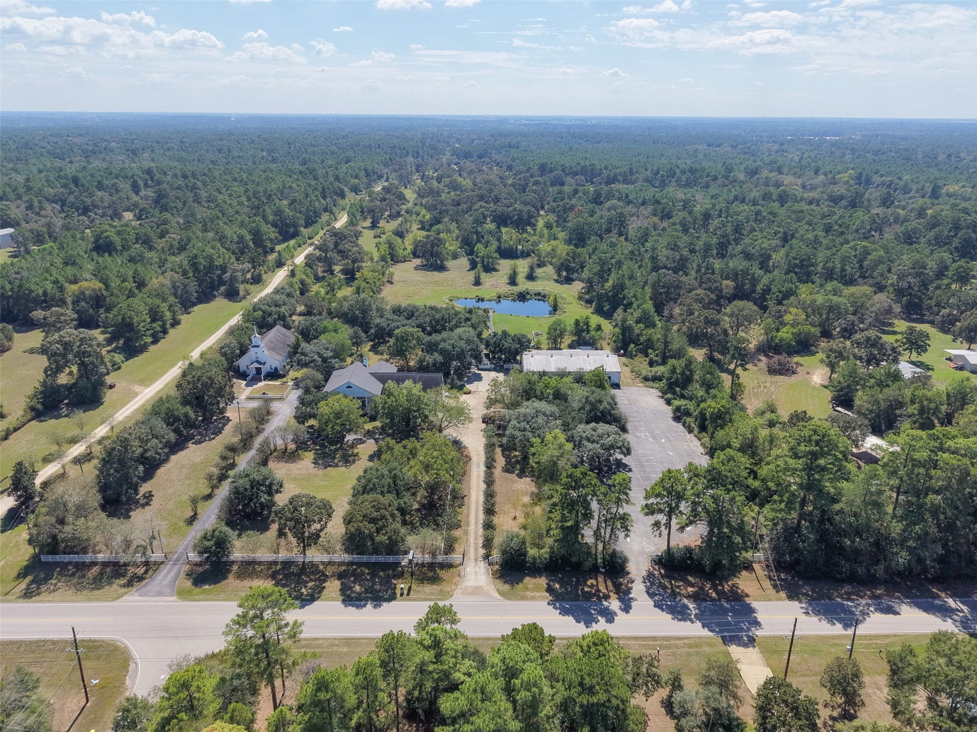Wide aerial perspective highlights the arrangement of buildings, parking areas, tree-lined grounds, and surrounding countryside.