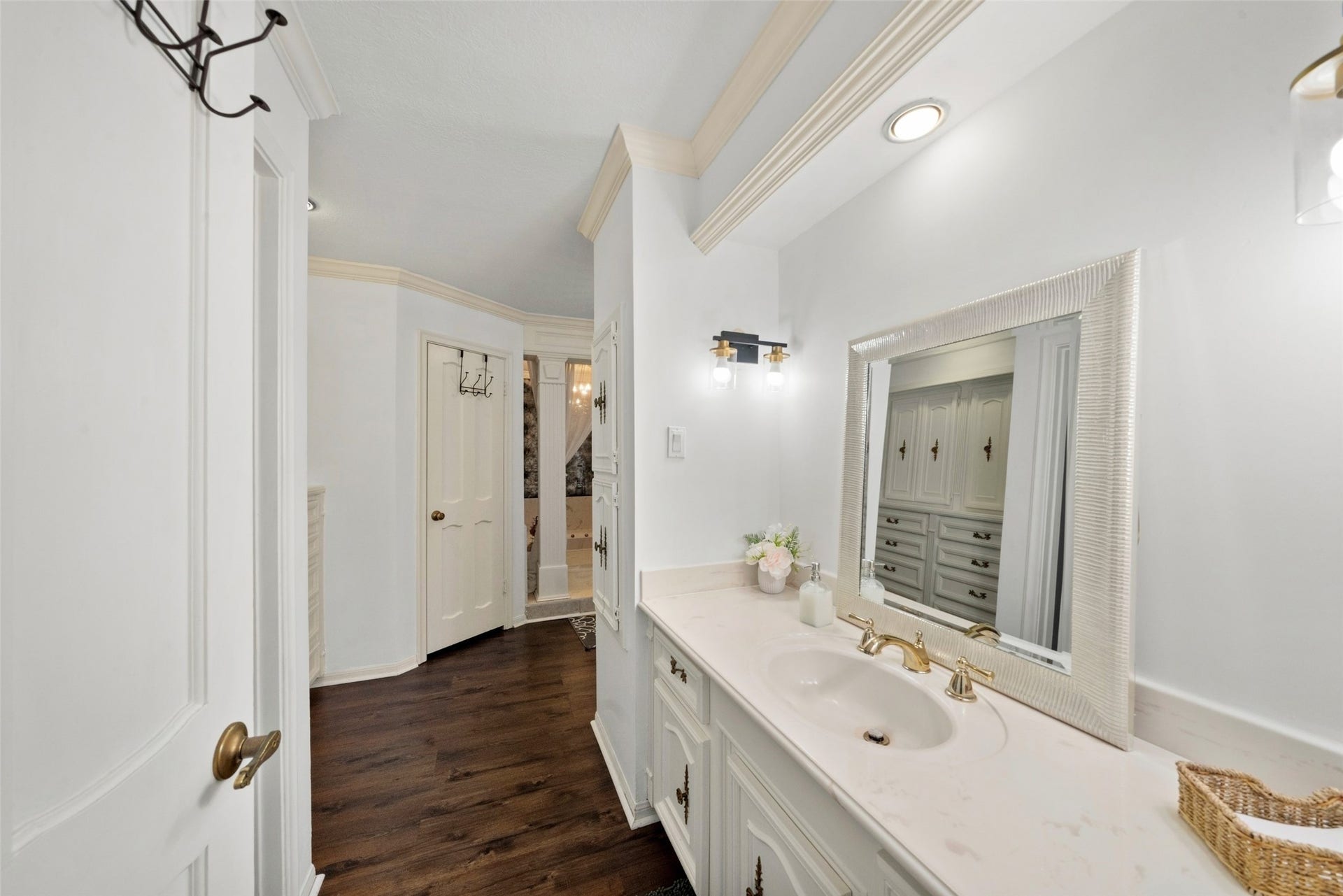 Alternate view of the bathroom with the sunken soaking tub, showcasing an extended vanity, large mirrors, white cabinetry, and wood flooring.
