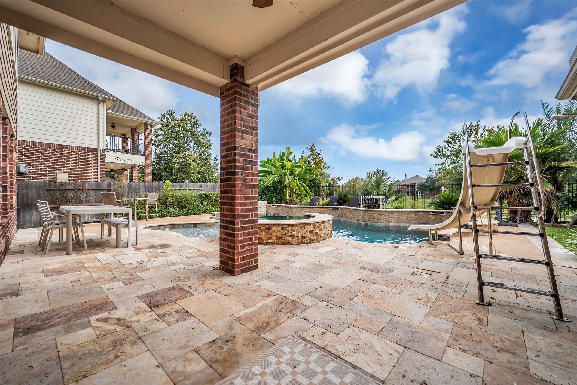 7907 Dunlap Field Lane, Richmond, TX 77407 Exceptional outdoor sanctuary featuring elegant stone decking, a shaded patio lounge, and a sparkling pool and spa combo framed by mature landscaping.