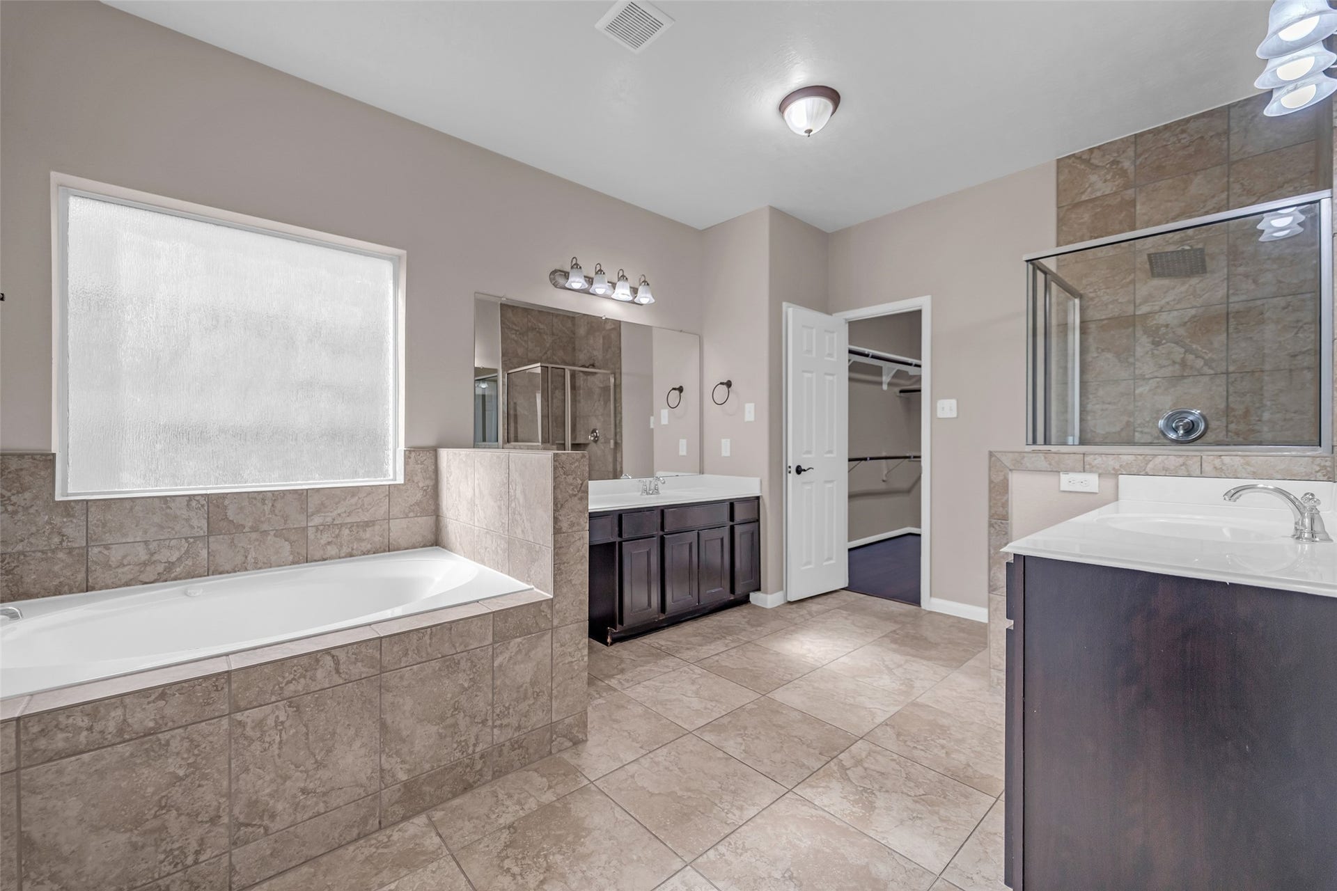 7907 Dunlap Field Lane, Richmond, TX 77407 Luxurious retreat highlighting dual vanities, a separate glass shower, and an inviting soaking tub, complemented by stylish tile work and bright, sunlit windows.