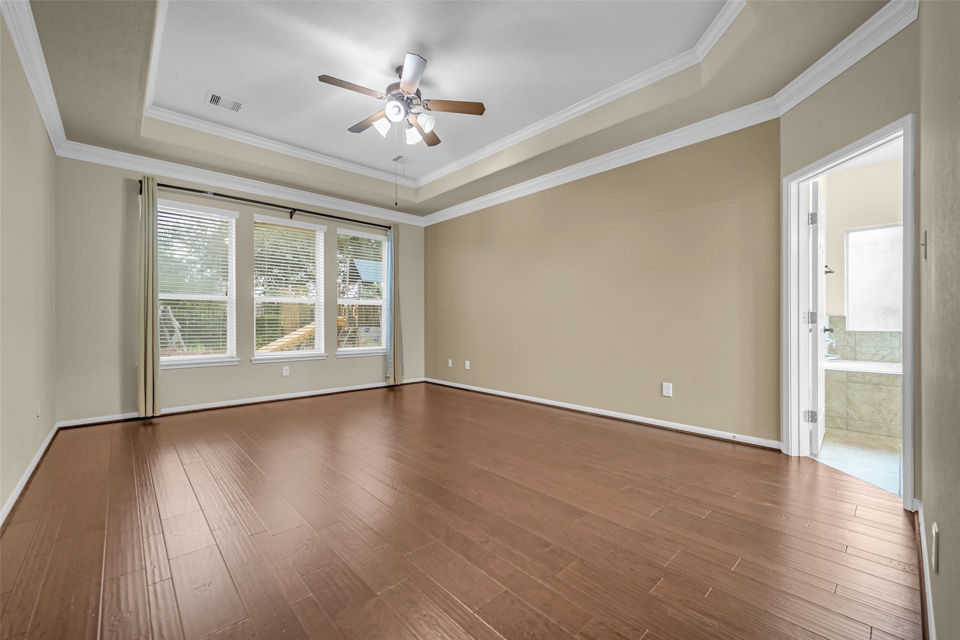 7907 Dunlap Field Lane, Richmond, TX 77407 This spacious primary suite features an elegant tray ceiling, warm wood flooring, and large windows that fill the space with natural light, creating a serene and restful retreat.