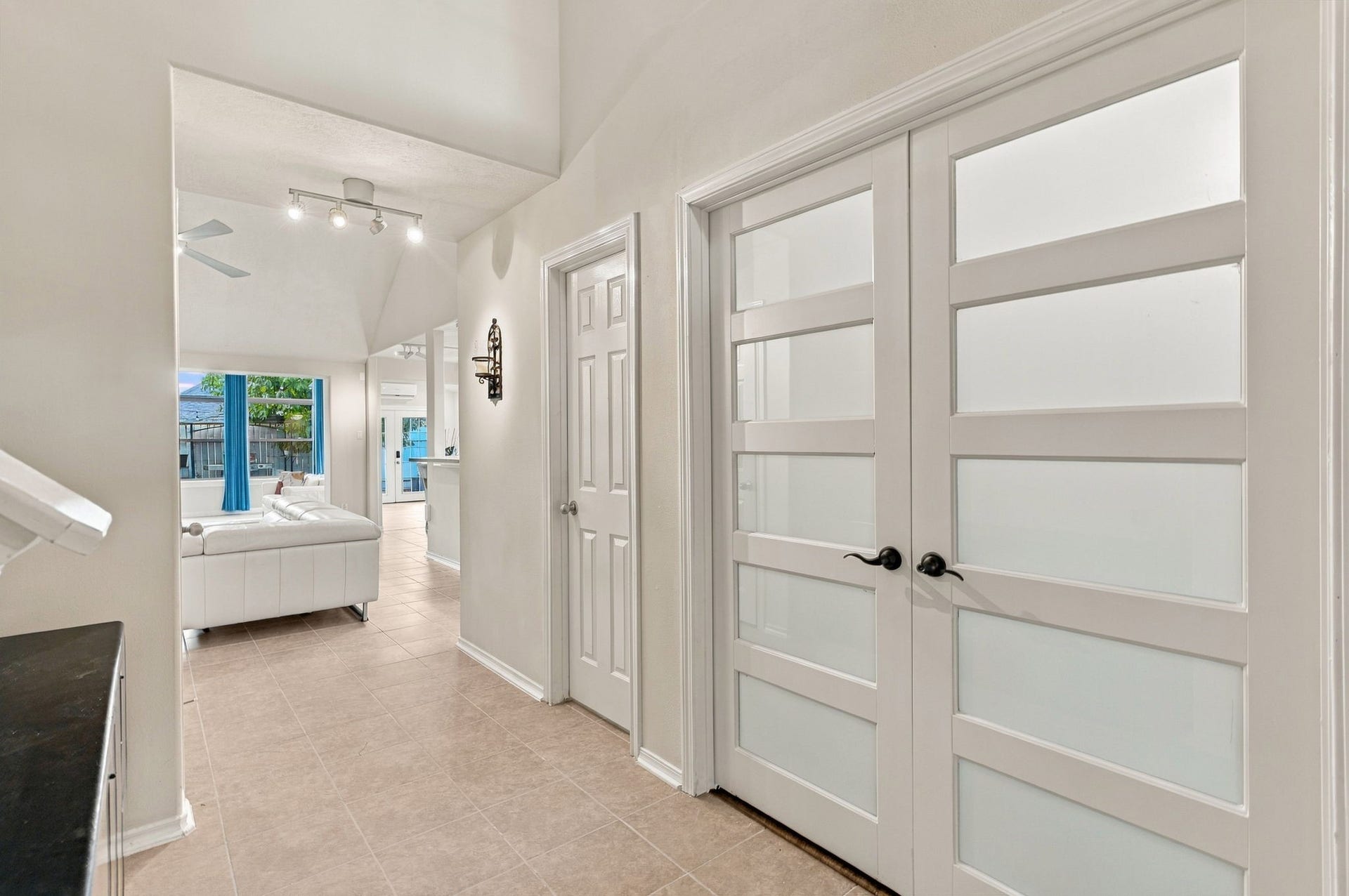 Elegant entryway with modern frosted glass doors leading to a bright, open living area featuring high ceilings and stylish tile flooring.