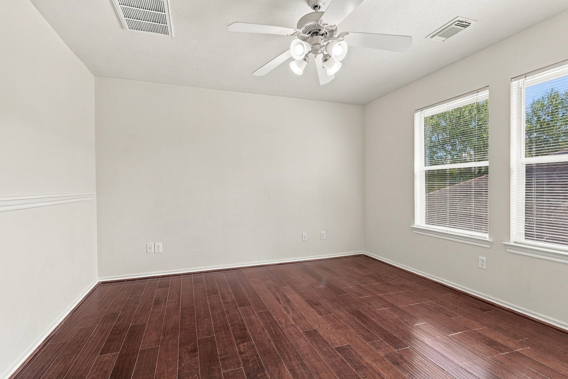 Bright and airy room featuring rich hardwood floors, large windows, and a modern ceiling fan for comfort and style.