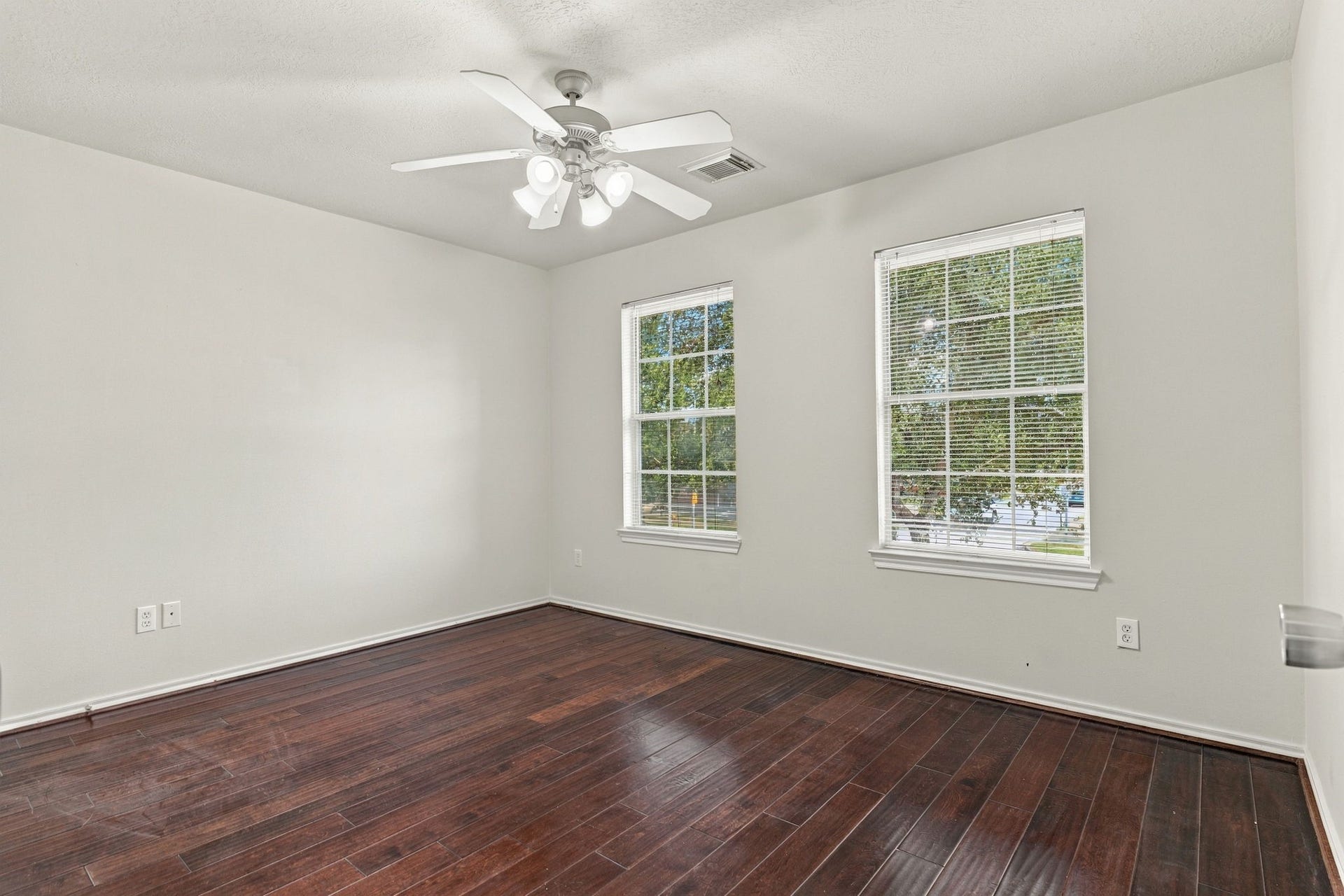 Bright and airy room featuring rich hardwood floors, dual windows for ample natural light, and a ceiling fan for comfort.