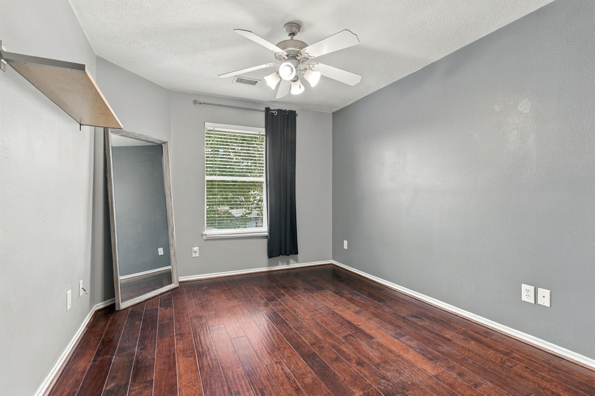 Charming room with rich hardwood floors, a sleek ceiling fan, and a large window that fills the space with natural light.