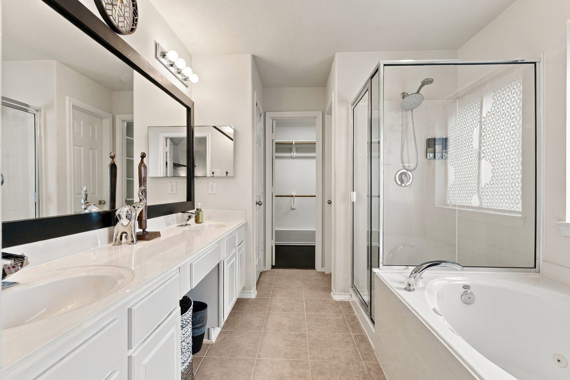 Spacious and elegant bathroom featuring a dual-sink vanity, a glass-enclosed shower, and a luxurious soaking tub, complemented by ample natural light and modern fixtures.