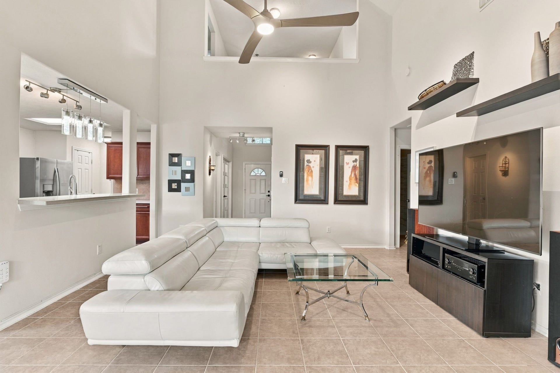 Spacious living area with high ceilings and modern design, featuring a sleek white sectional, large flat-screen TV, and open access to the kitchen, perfect for entertaining.