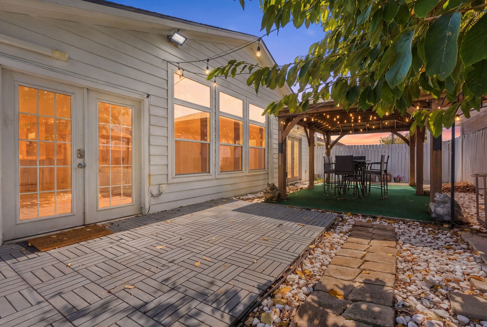 Charming backyard oasis featuring a spacious patio with elegant French doors, a cozy pergola adorned with string lights, and a stylish outdoor dining area, perfect for entertaining.