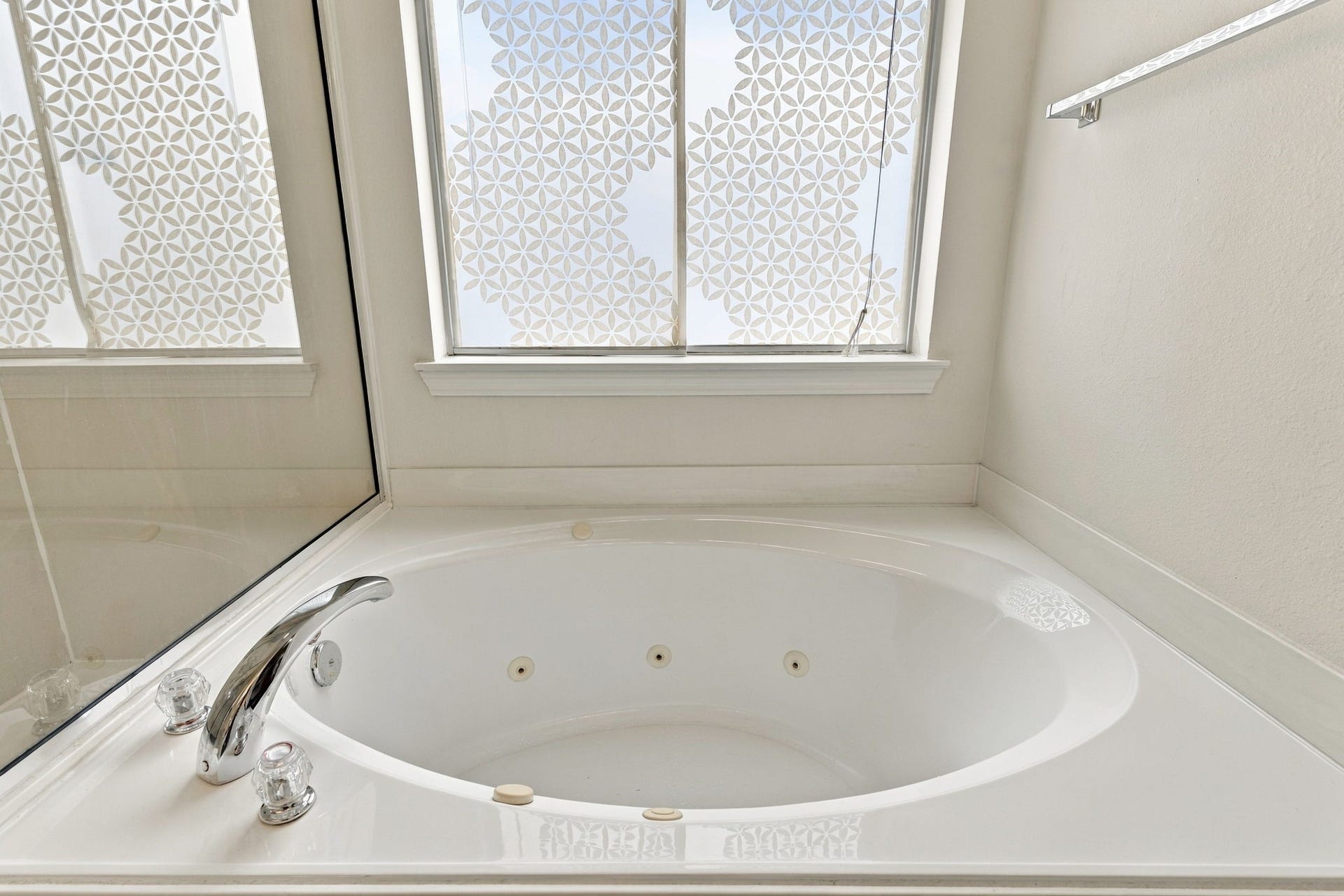 Luxurious Jacuzzi tub with elegant fixtures, complemented by a beautifully patterned privacy window for a serene bathing experience.